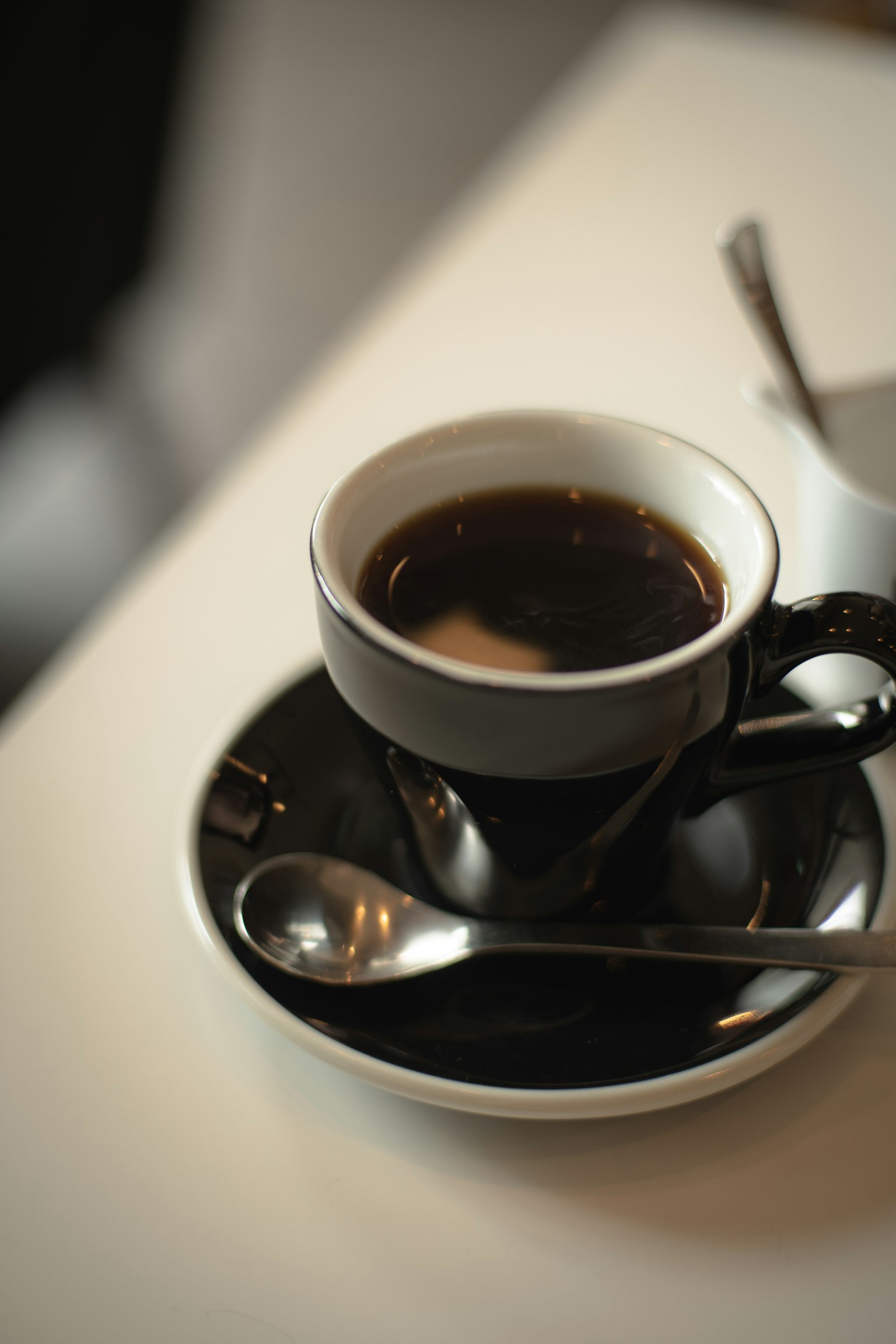 Cốc cà phê đen nóng trên đĩa đen với thìa bạc