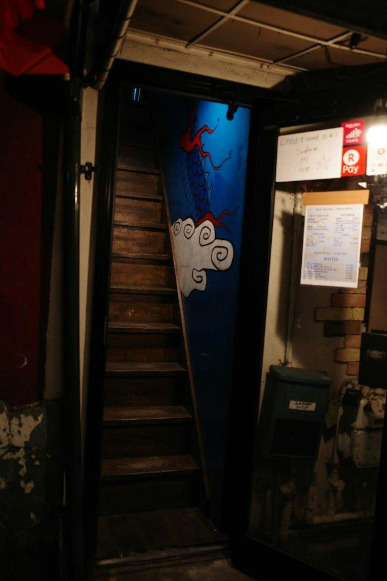 A dark corridor leading up a staircase with blue wall art and white cloud design