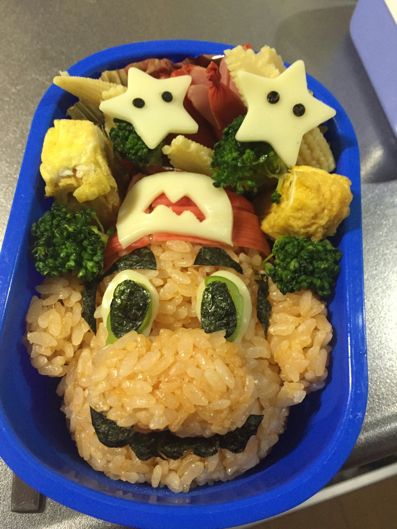 Una scatola bento con il volto di un personaggio fatto di riso e verdure