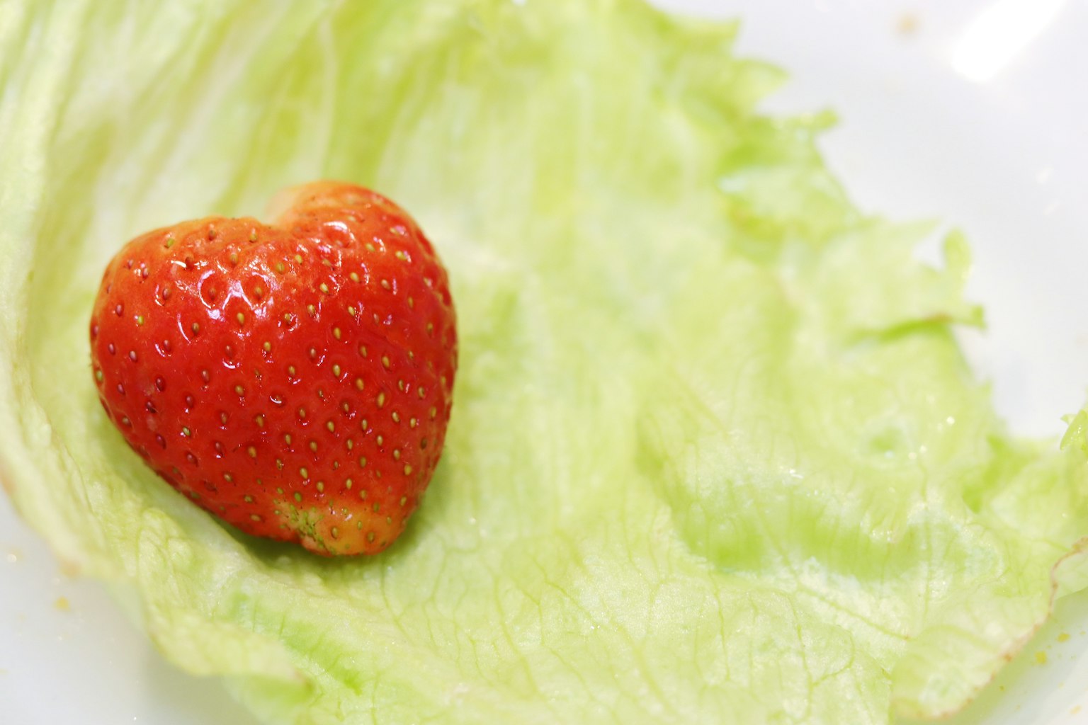 Eine herzförmige Erdbeere auf einem grünen Salatblatt