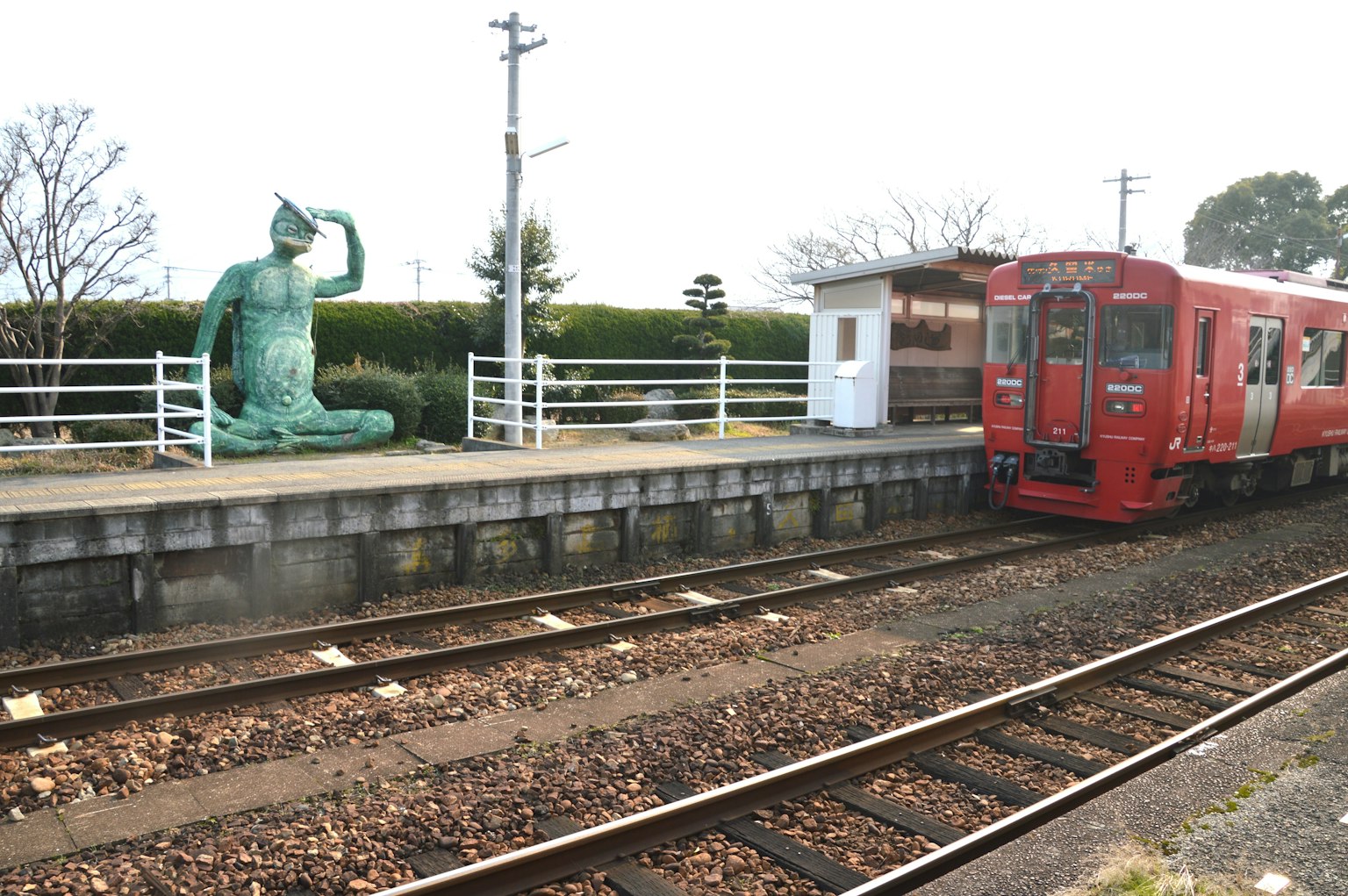 A red train at a station with a bronze statue nearby