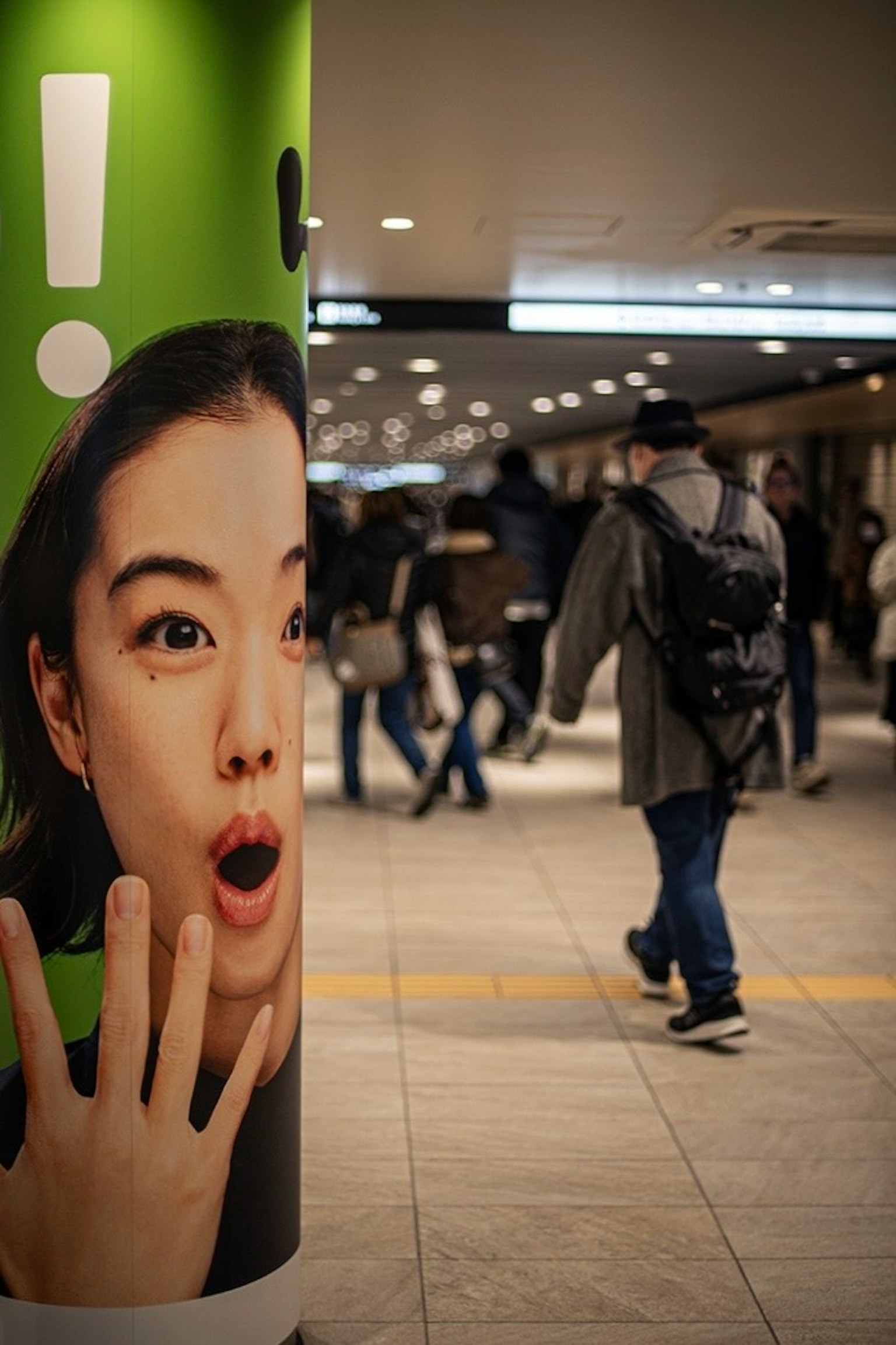 一个惊讶的女性面孔在繁忙车站的绿色柱子上