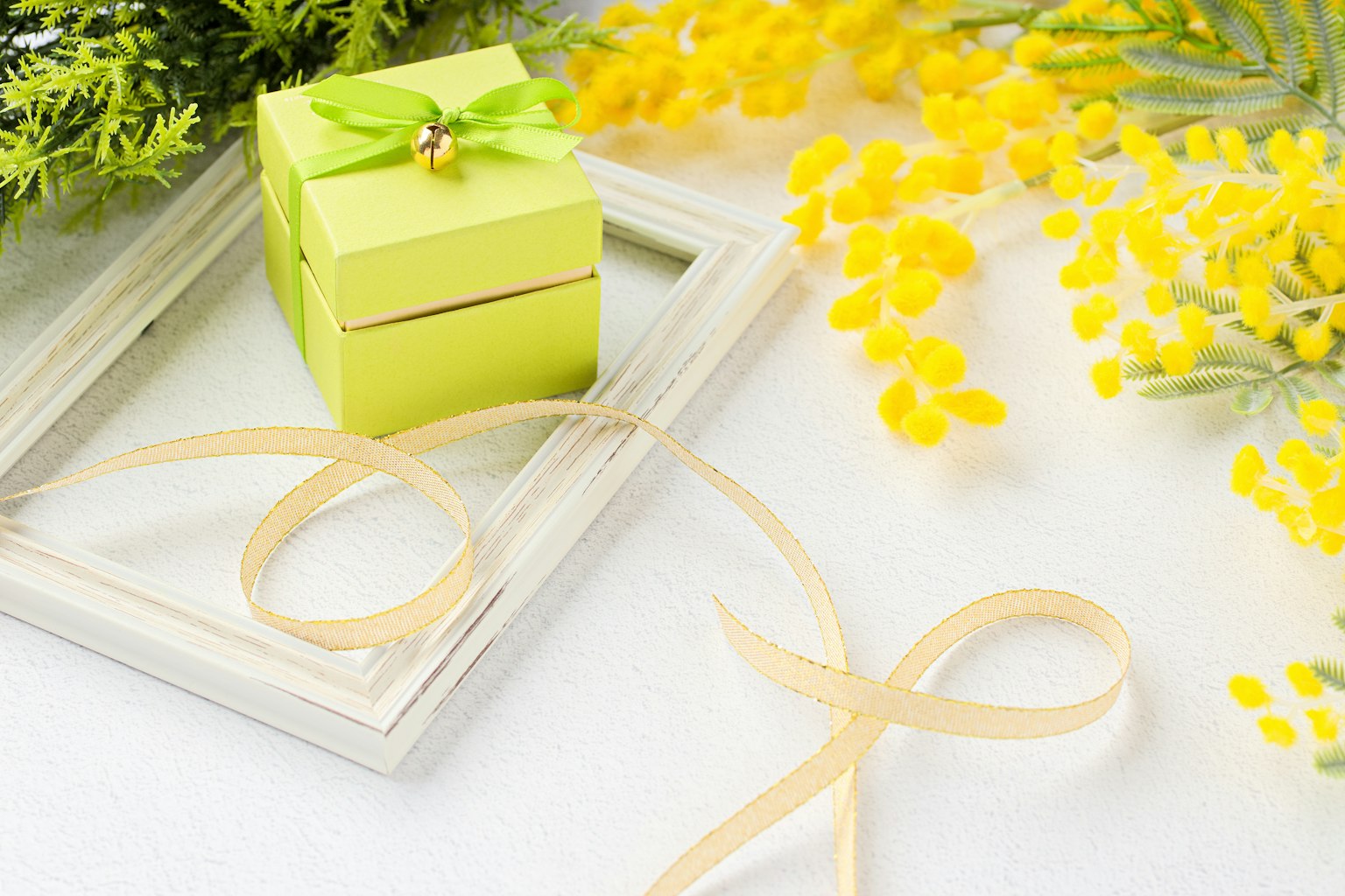 Gambar yang menampilkan kotak hadiah hijau kecil dikelilingi bunga mimosa kuning