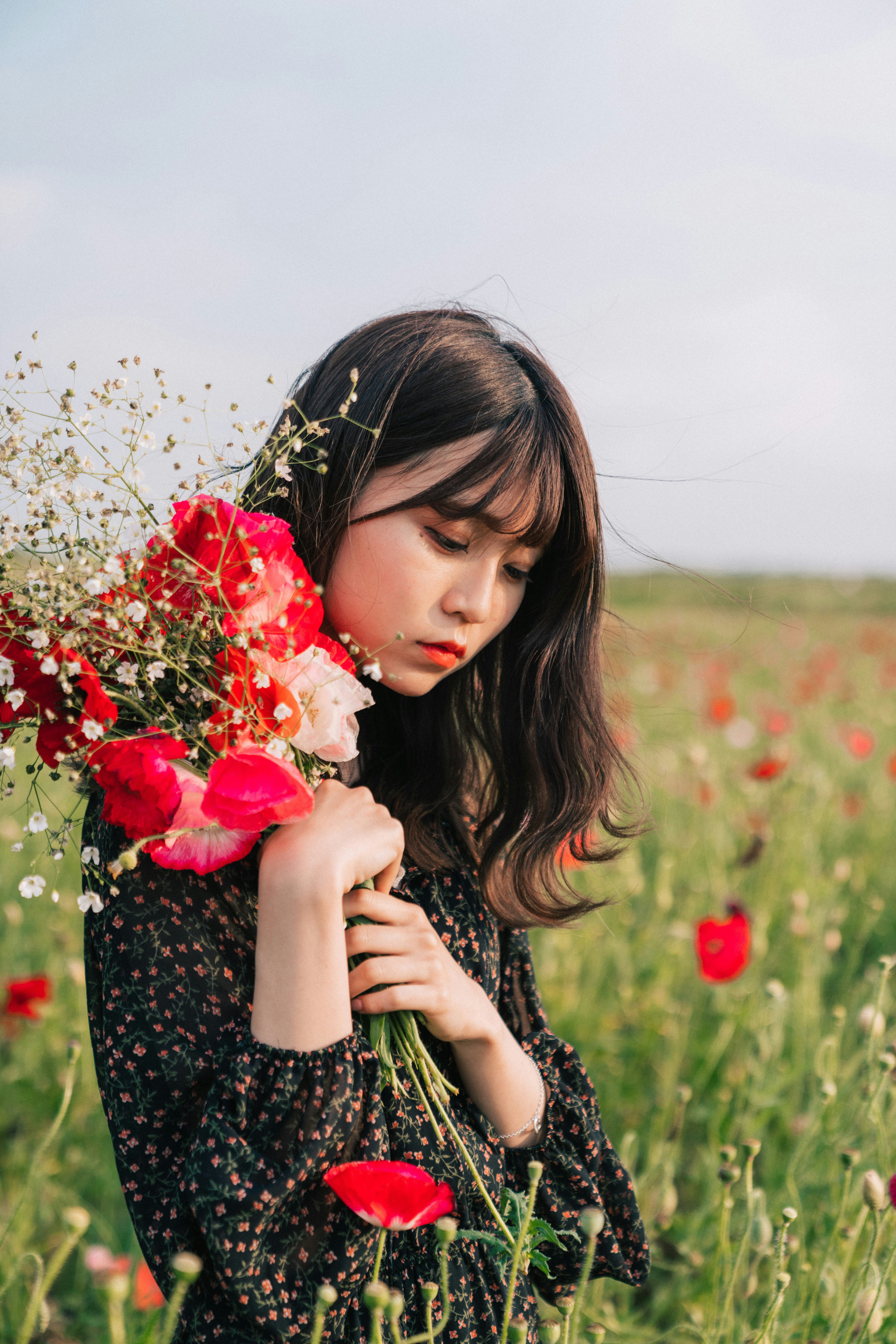 người phụ nữ cầm bó hoa đỏ trong cánh đồng hoa