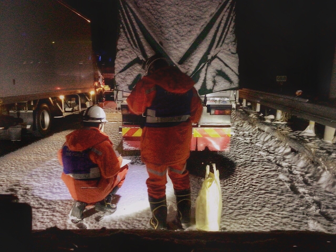 雪の降る国道で走行不能になった車の前に立つ作業員