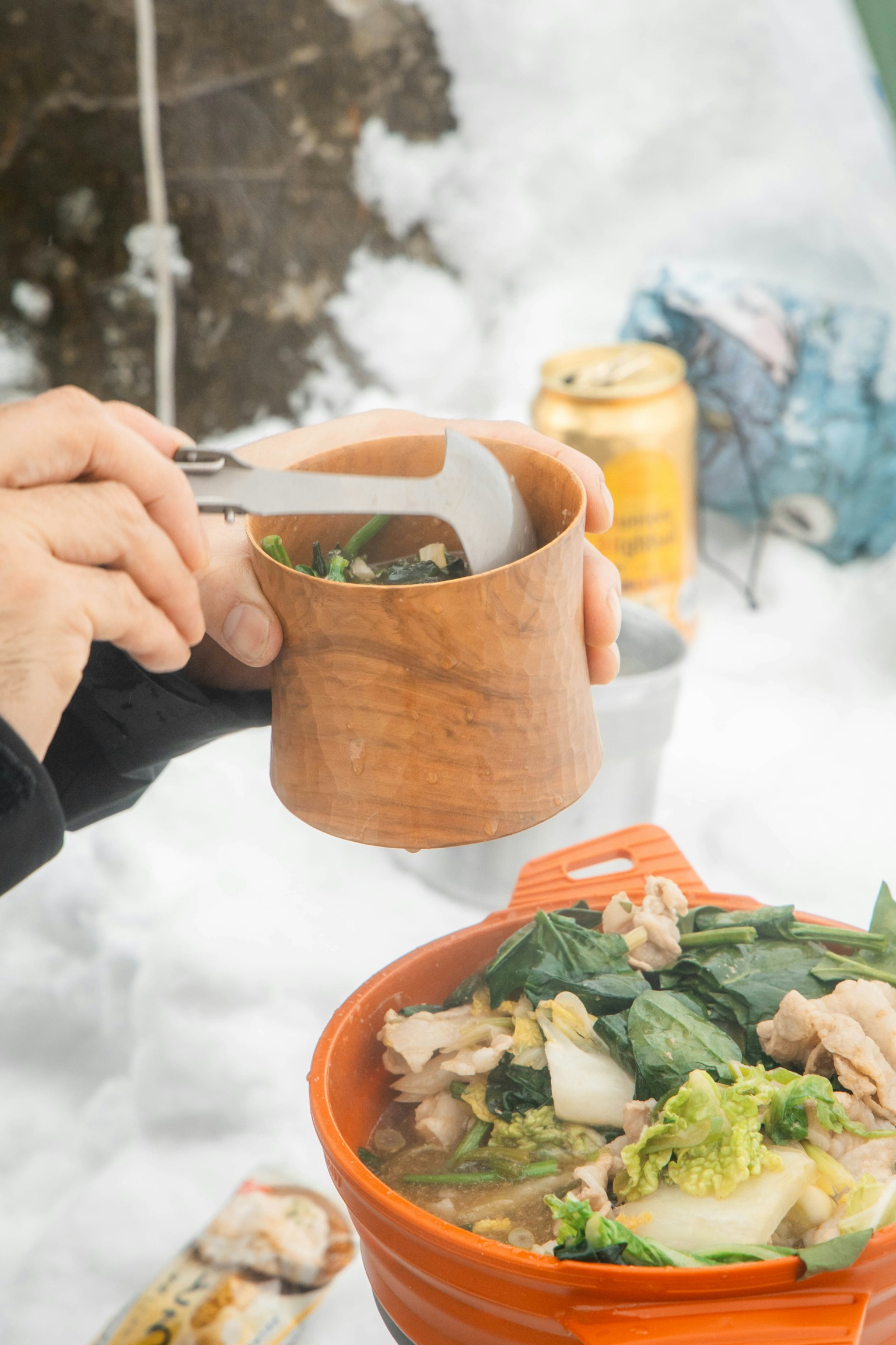 Hand holding a wooden cup while enjoying soup in the snow