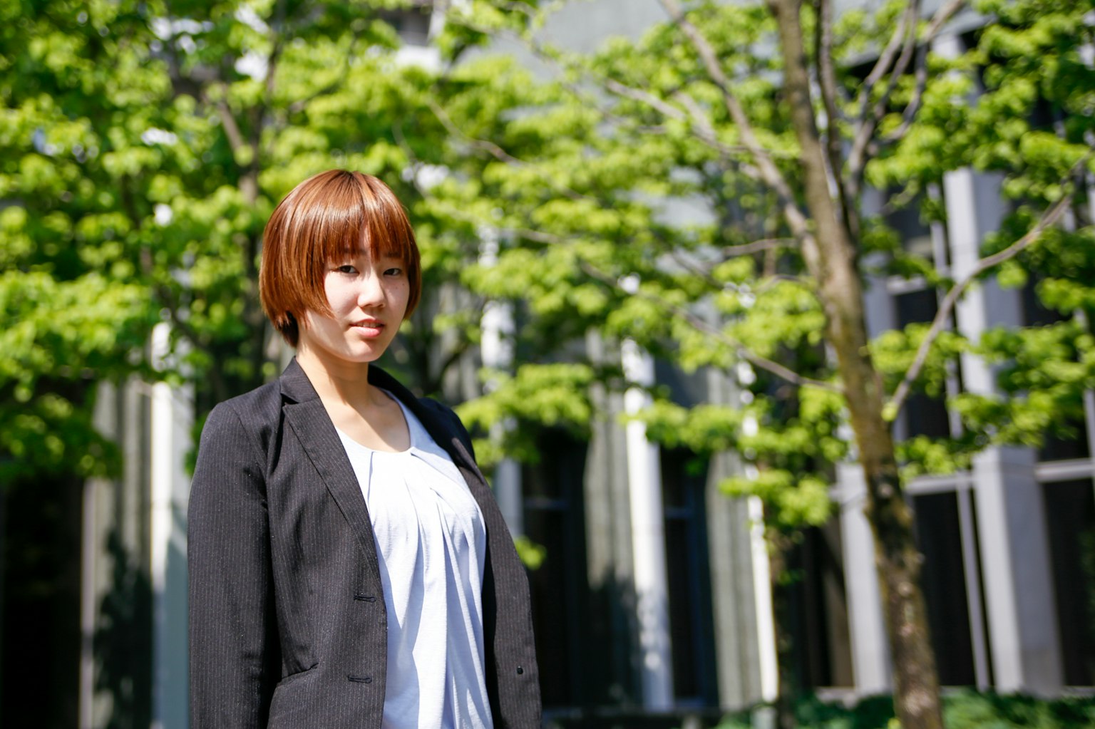 Portrait d'une femme debout devant des arbres verts avec des cheveux courts et portant un costume