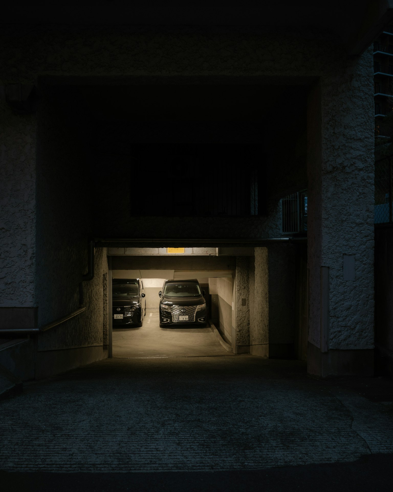 Dos coches estacionados en la entrada de un garaje con poca luz y luz ambiental