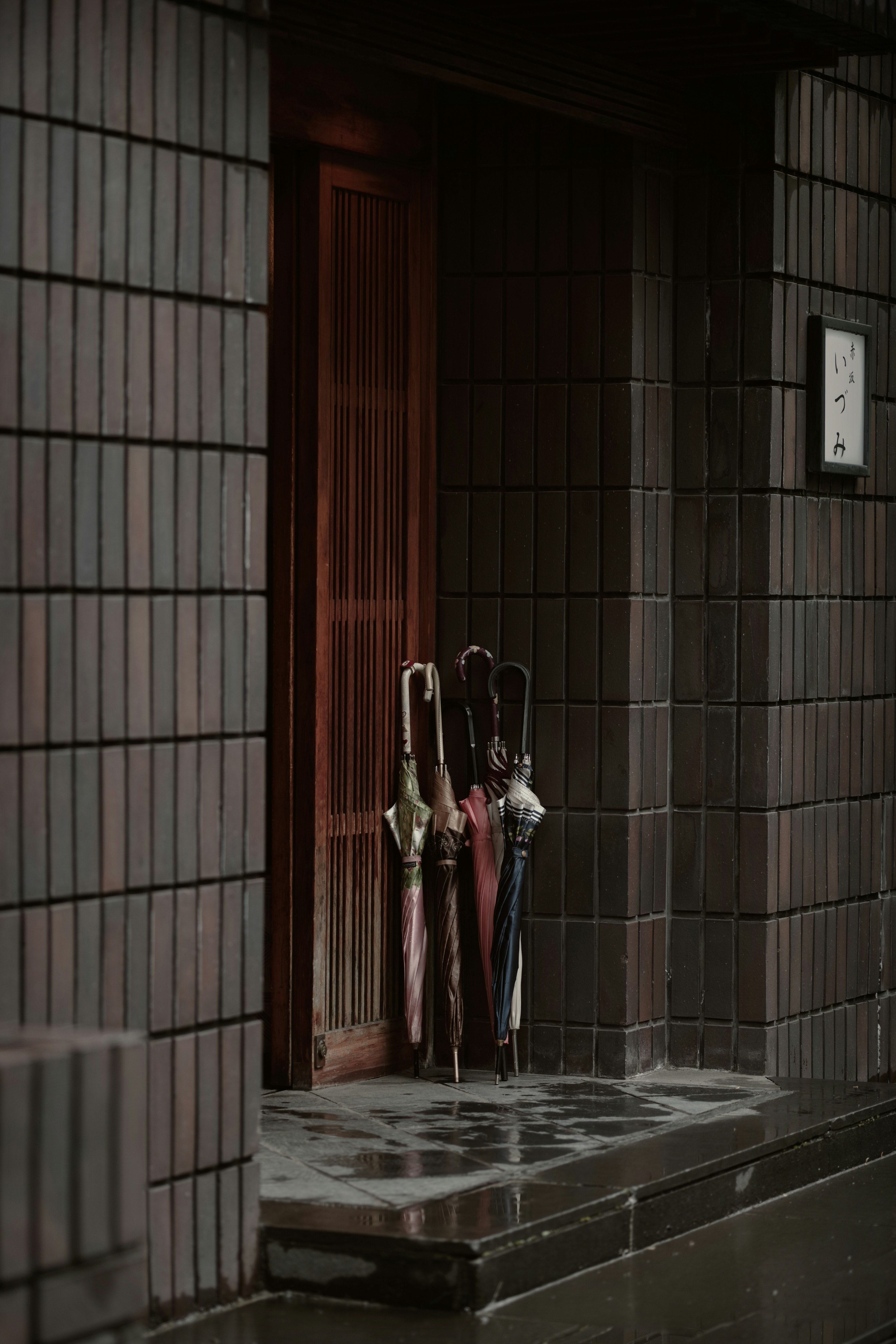 People with umbrellas gathering at a storefront in rainy Tokyo alleyway