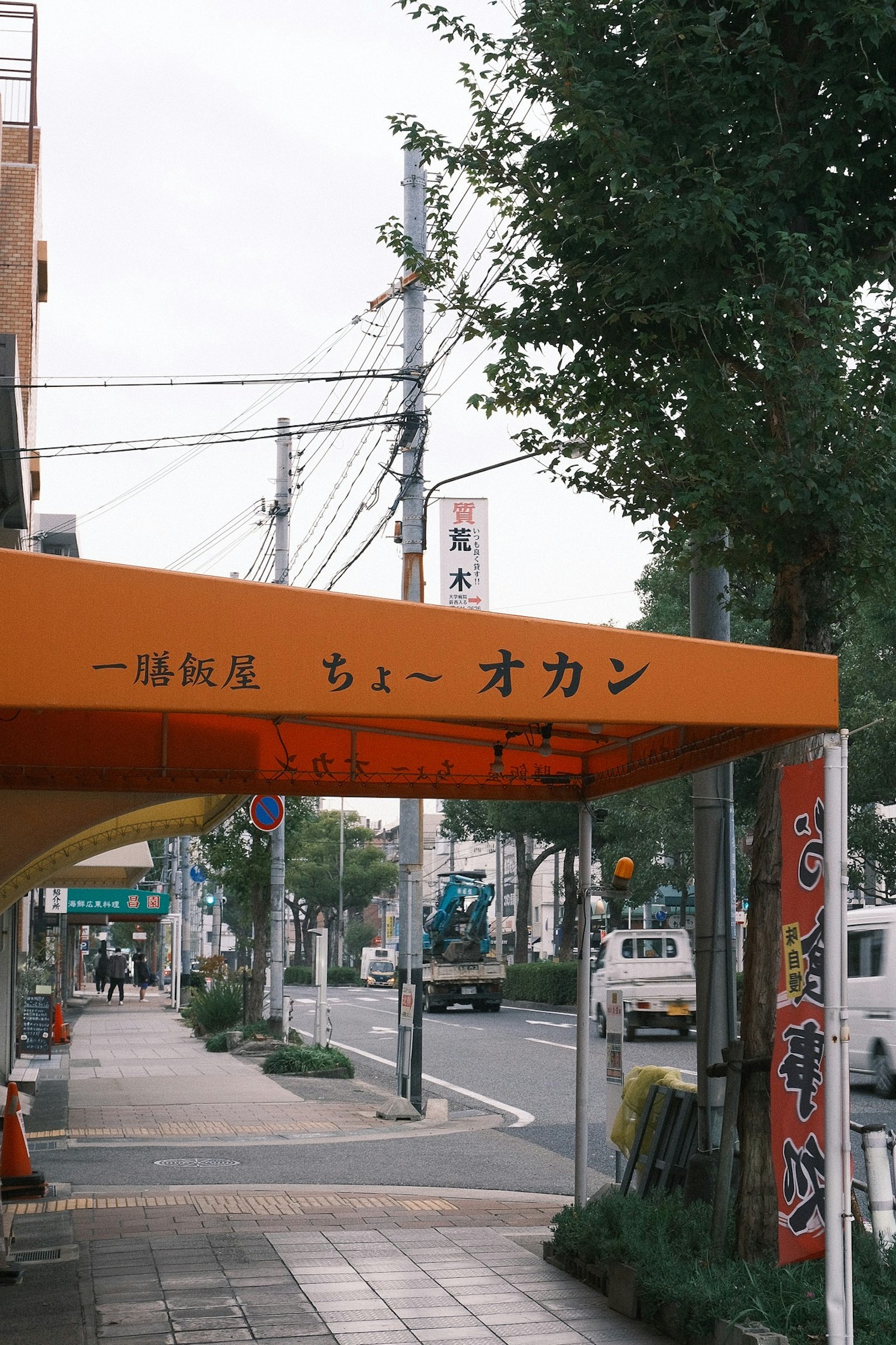 Pemandangan jalan dengan papan tanda oranye yang menunjukkan nama toko dalam bahasa Jepang