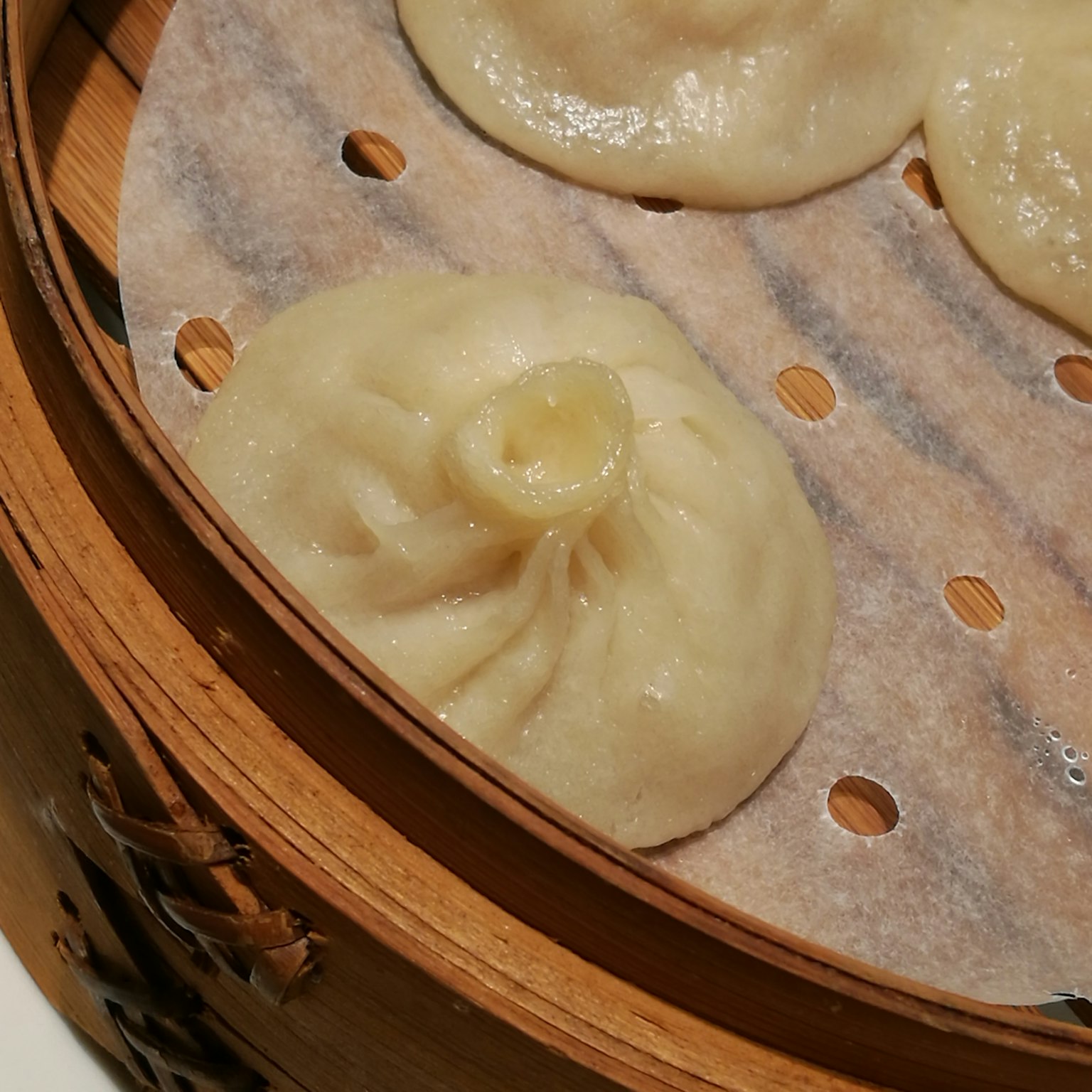 Close-up xiaolongbao dalam kukusan adonan mengkilap dan isian berair