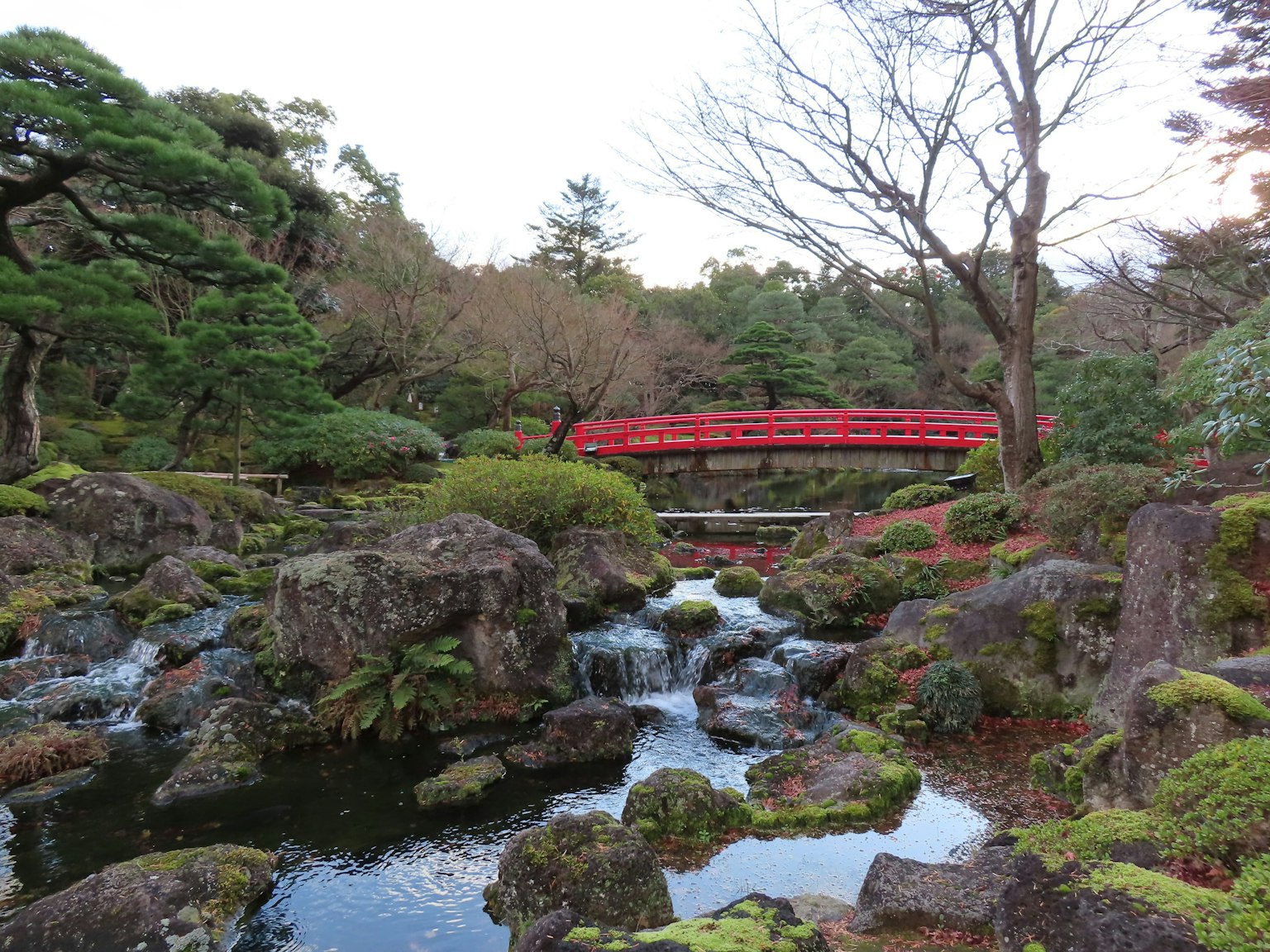 ทิวทัศน์สวนญี่ปุ่นที่สวยงาม สะพานสีแดงเหนือสายธารล้อมรอบด้วยก้อนหิน มอสสีเขียวบนหิน