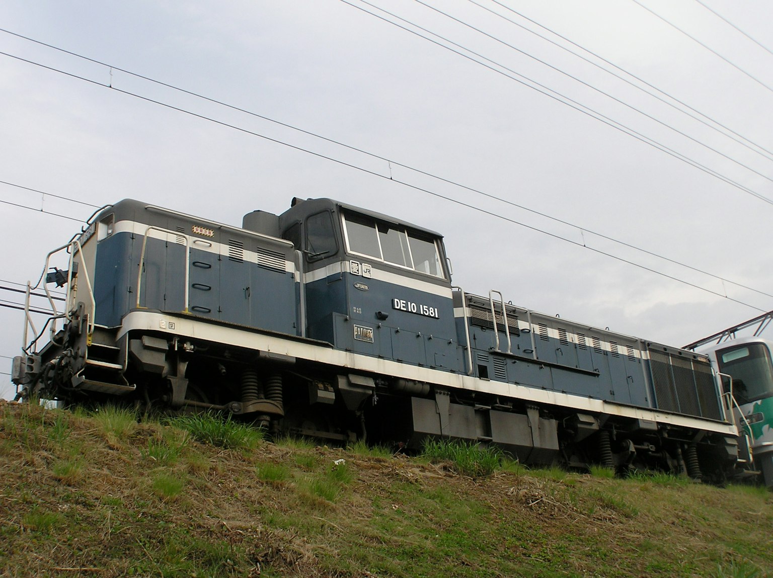 Locomotora azul estacionada en la hierba con líneas eléctricas al fondo