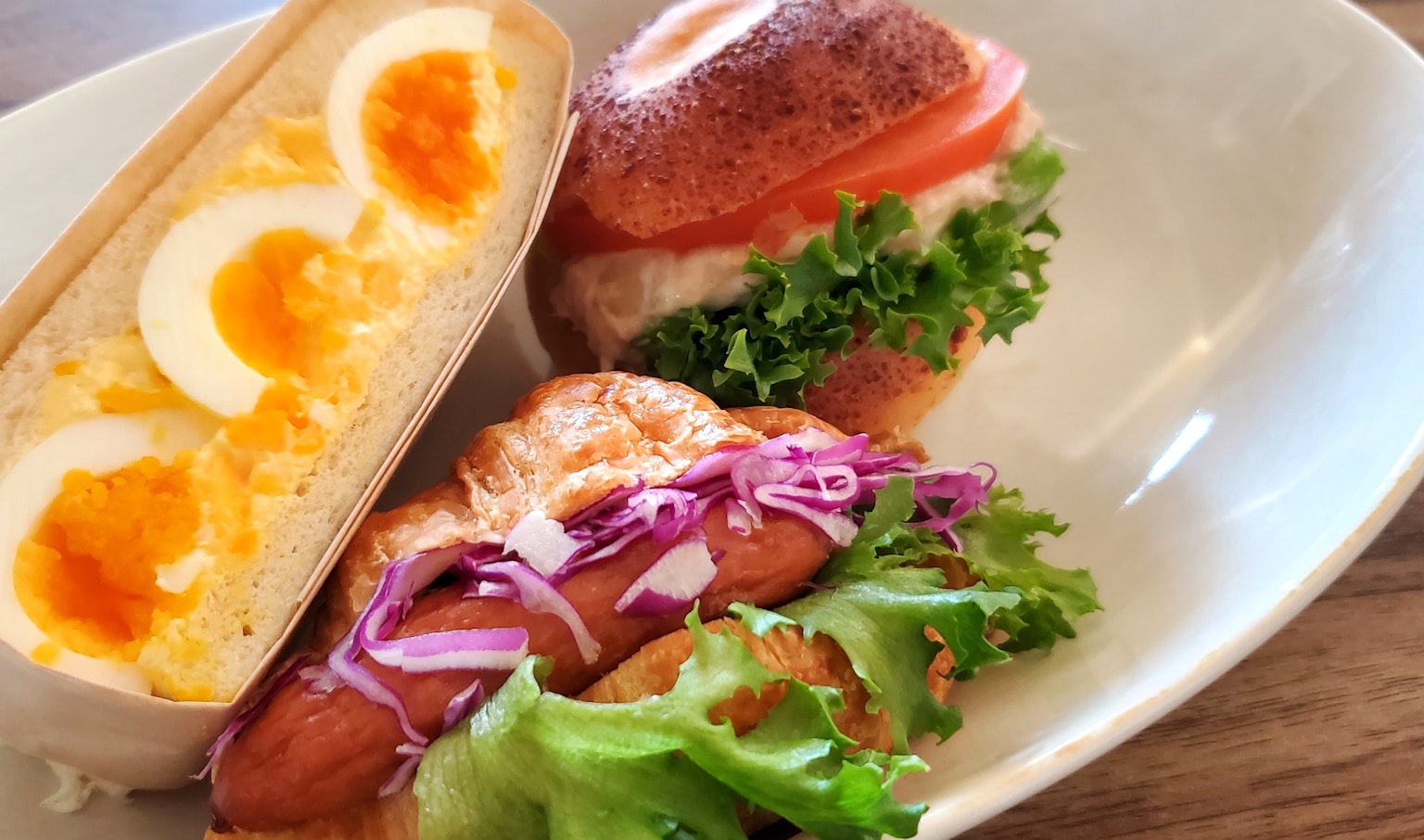 Un piatto con un panino farcito con uova e verdure accanto a un hot dog