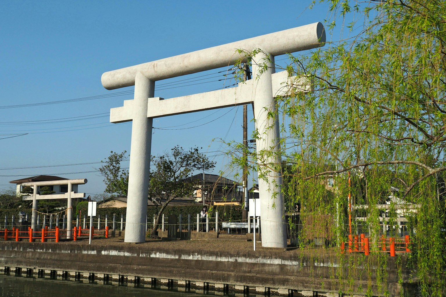 Large concrete torii gate under a blue sky with surrounding scenery
