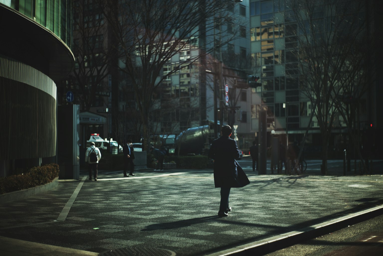 Silhouettes of people standing at a dimly lit street corner with contrasting shadows