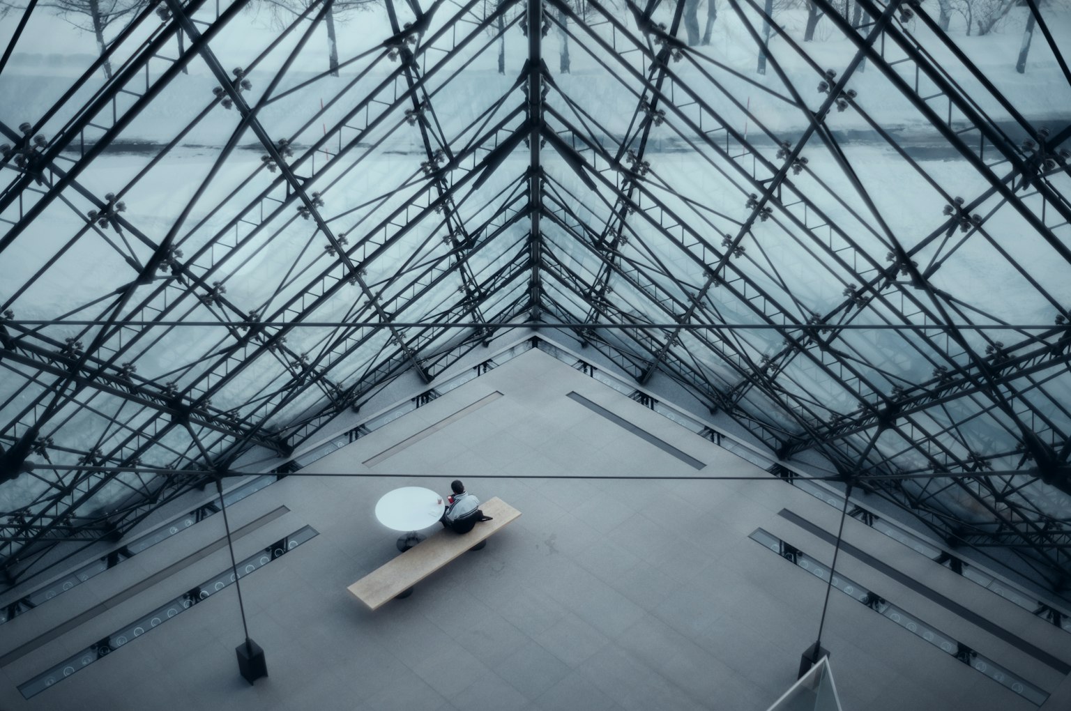 Interior de la pirámide del Louvre mostrando su estructura de vidrio y una mesa sencilla