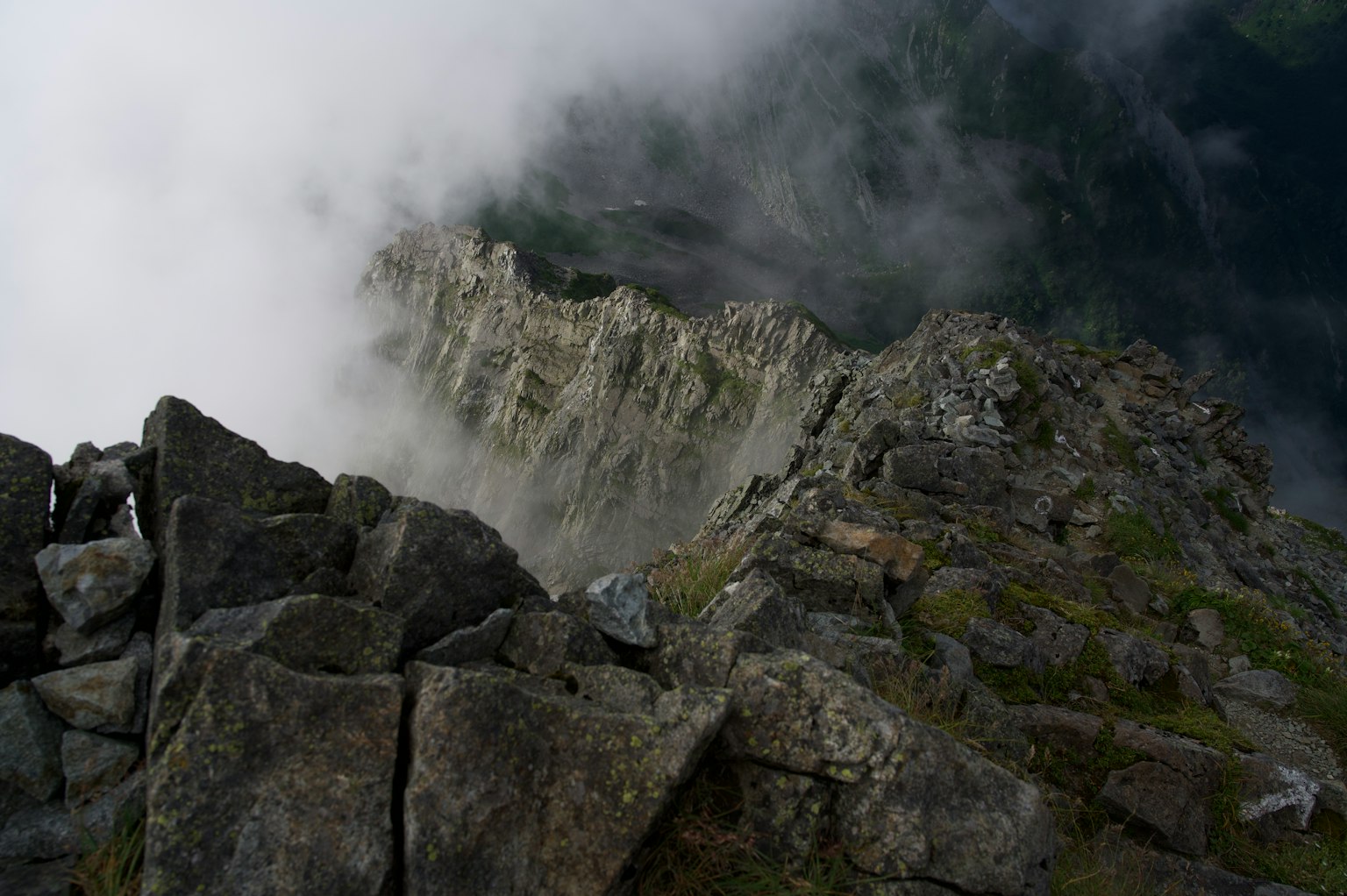 Vista desde la cima de la montaña cubierta de nubes con rocas y hierba verde
