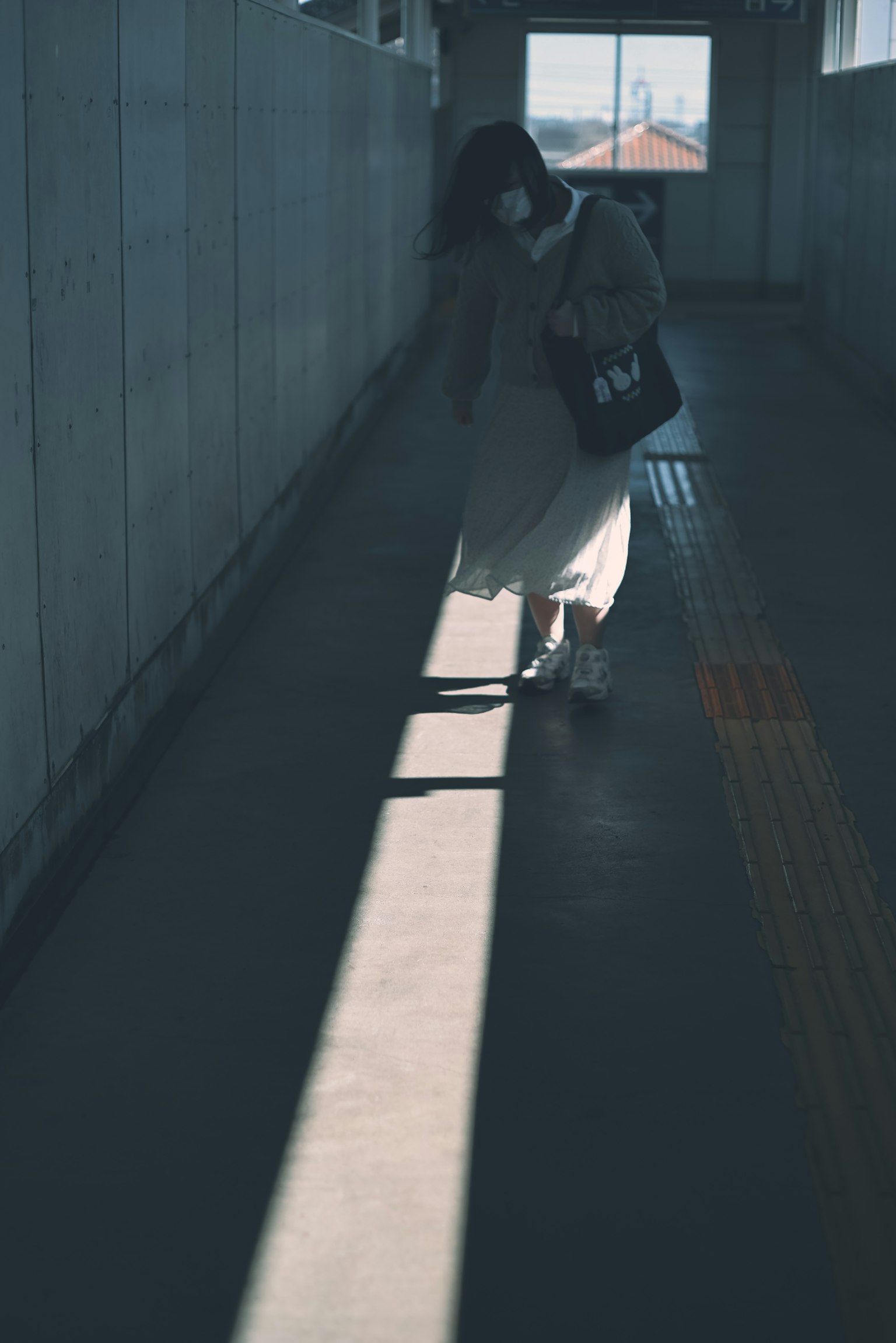 Donna che cammina nella luce fioca indossando un vestito bianco e portando una borsa nera in un corridoio