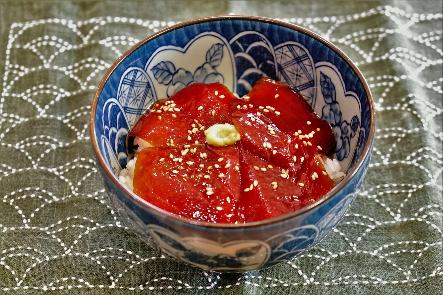 Una bella ciotola giapponese blu piena di sashimi rosso guarnito con semi di sesamo