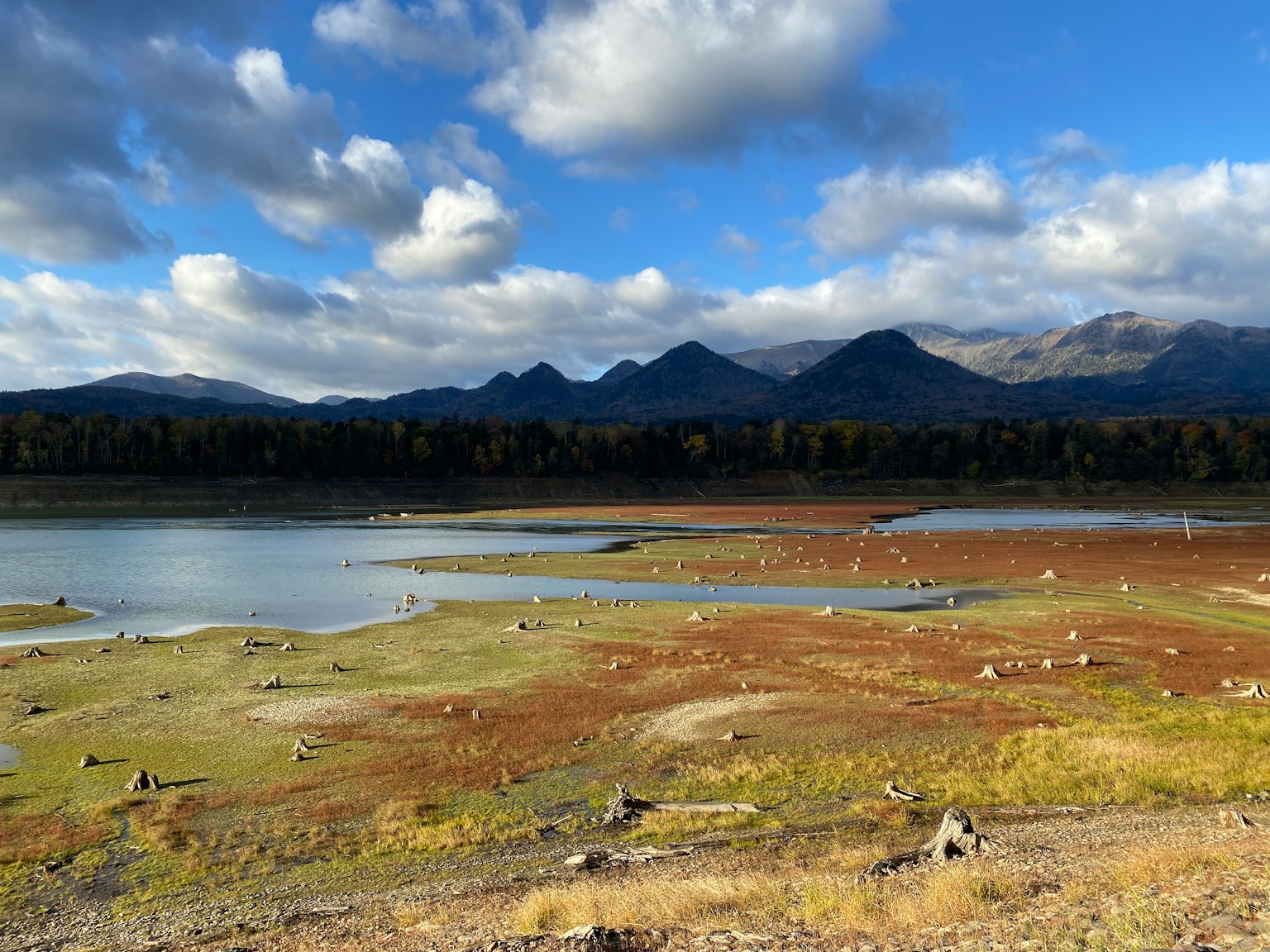 Vue pittoresque d'un lac entouré d'un ciel bleu et de nuages montagnes lointaines et terre sèche avec des rochers éparpillés
