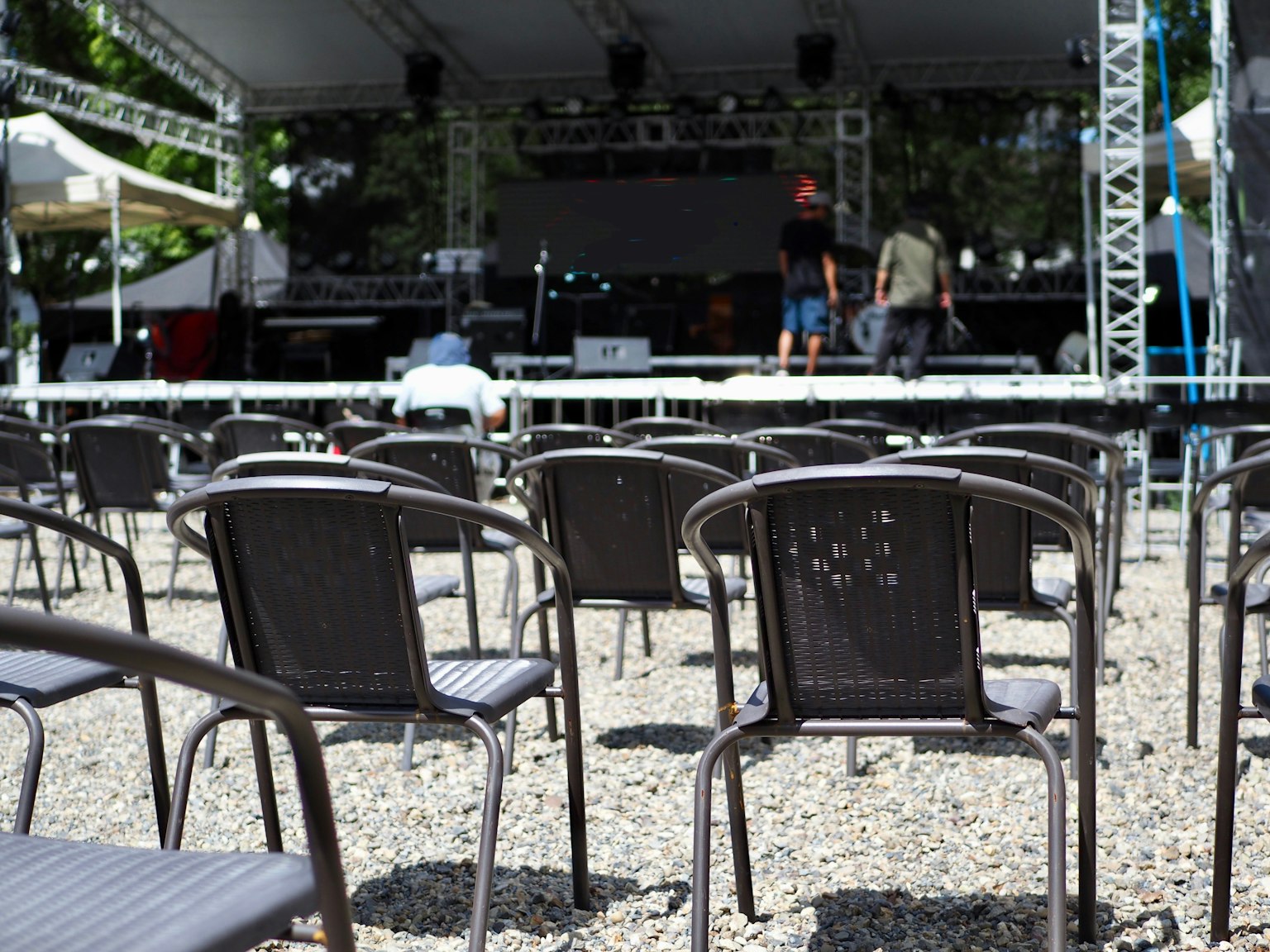 Black chairs lined up in front of a stage with an outdoor setup