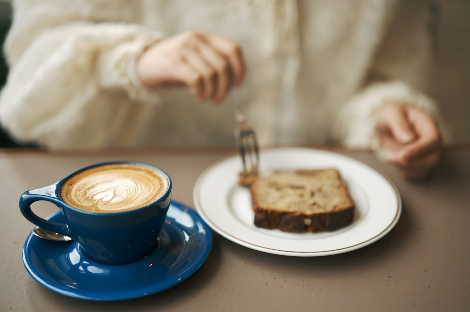 青いカップのコーヒーと白い皿に載ったパンのスライスを持つ手