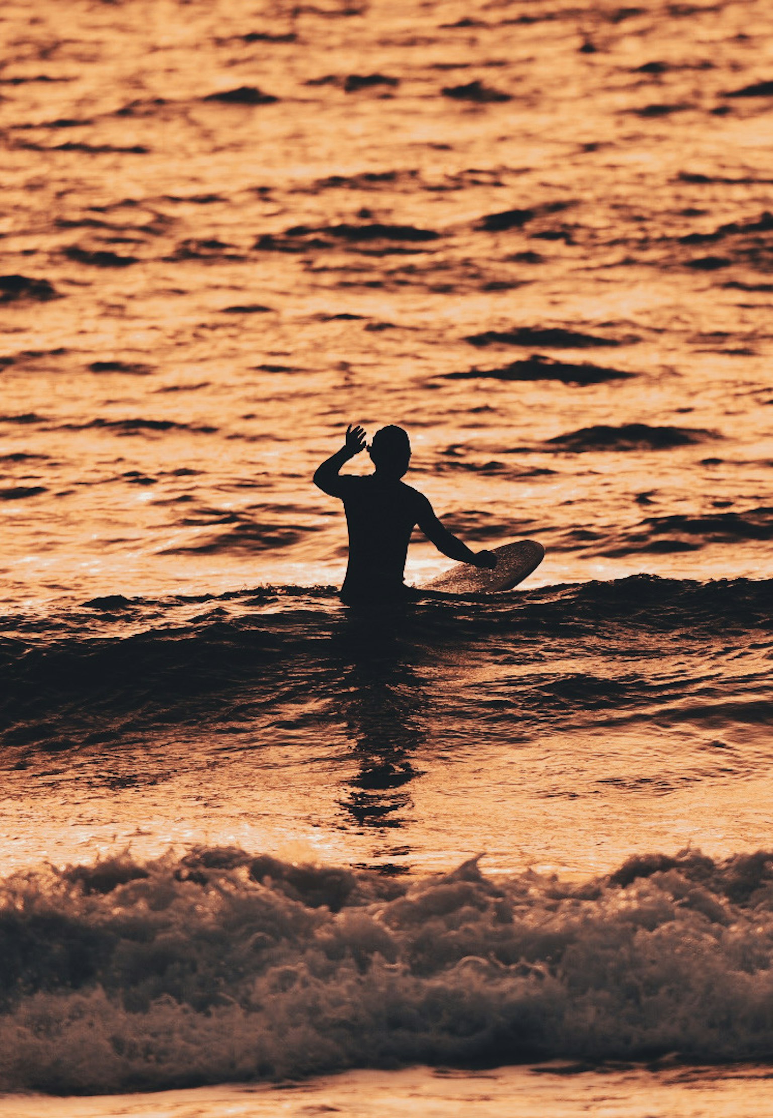 Silhouette di una persona che fa surf al tramonto nelle onde dell'oceano