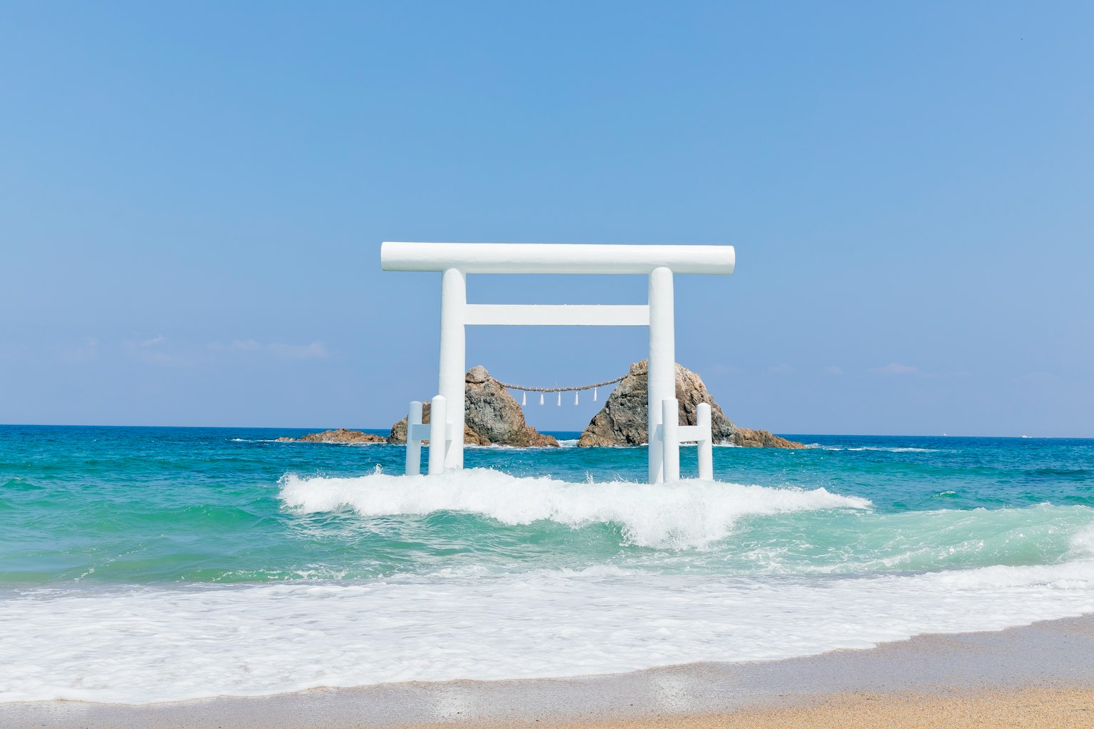 Pintu torii putih di lautan dengan batu di bawah langit biru