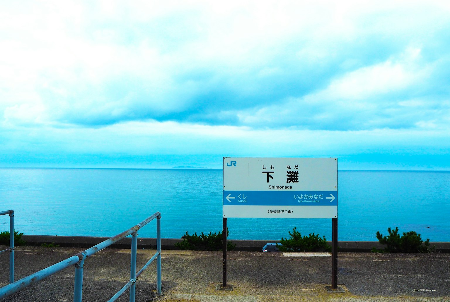 Schild der Station Shimonoseki mit blauem Meer und bewölktem Himmel