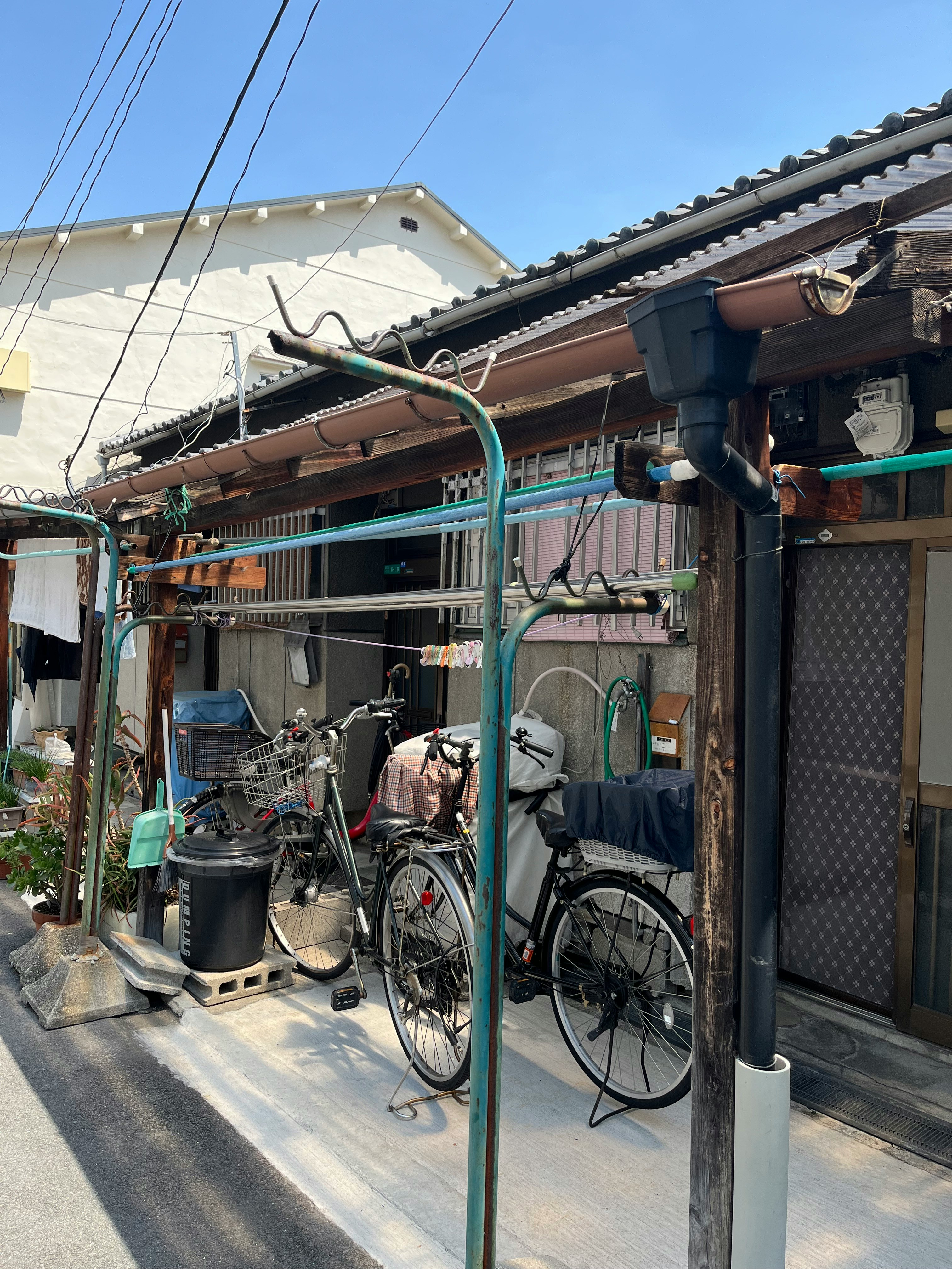 路地に並ぶ自転車と物干しのある住宅の軒先