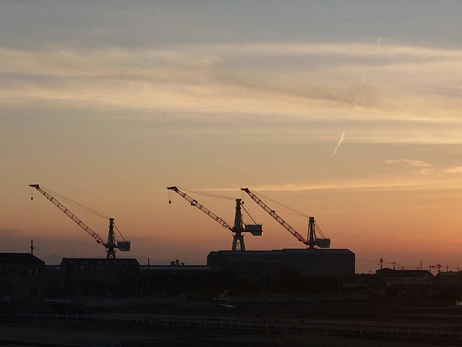 夕焼けの中にシルエットとして浮かぶクレーンと建設現場