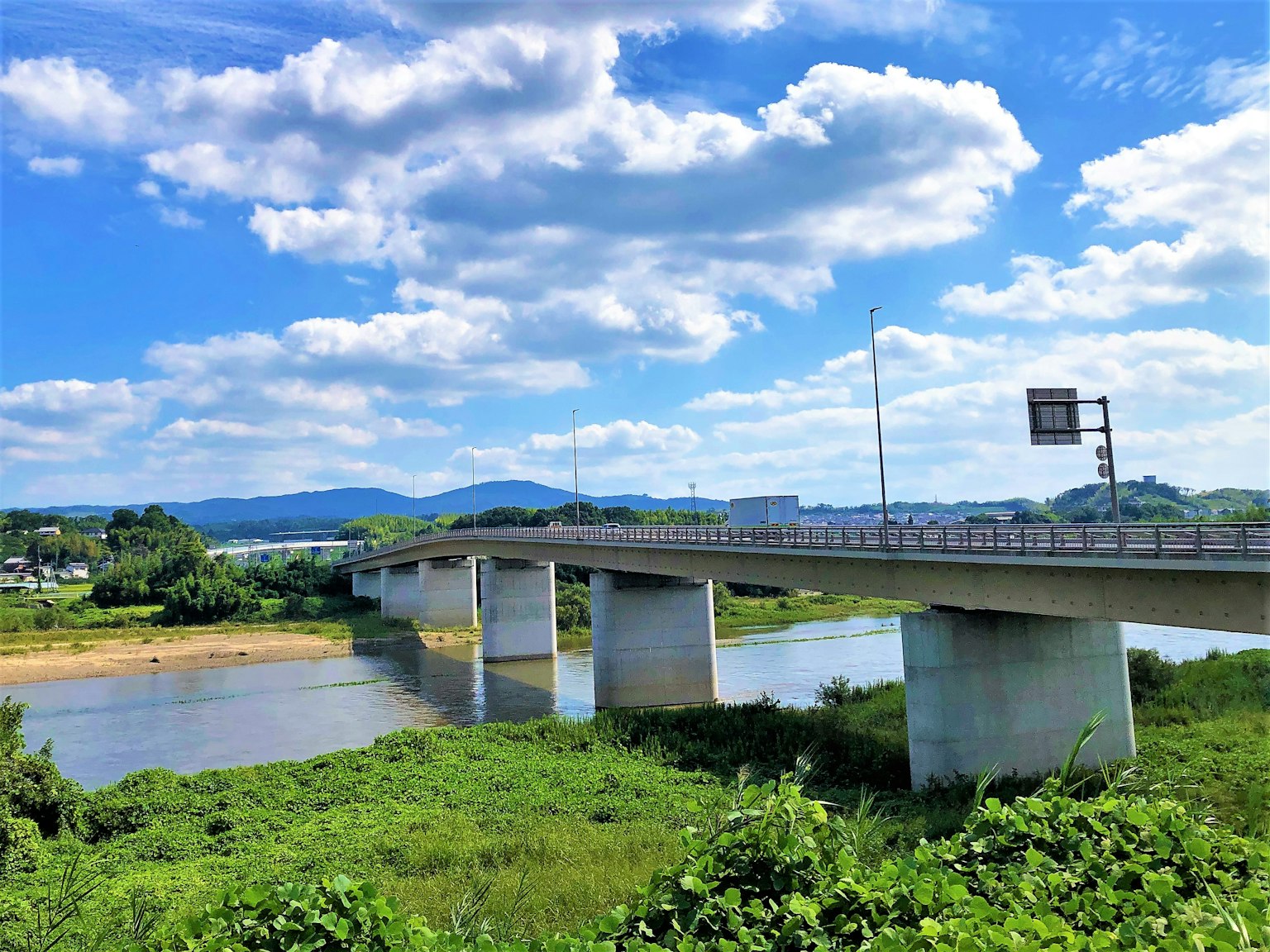 Jembatan di atas sungai dengan vegetasi subur dan langit biru