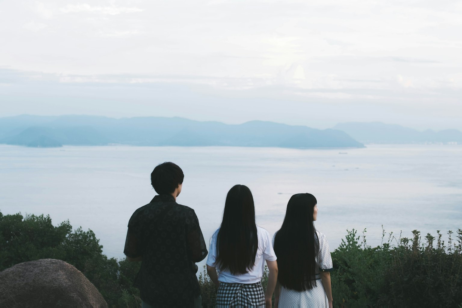 สามคนมองไปที่ทะเลพร้อมภูเขาในพื้นหลัง