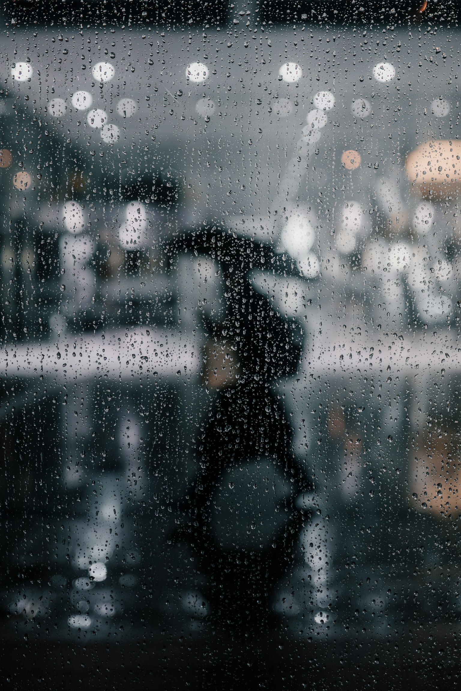 Hình bóng của một người nhìn qua cửa sổ ướt mưa nền mờ với các điểm sáng