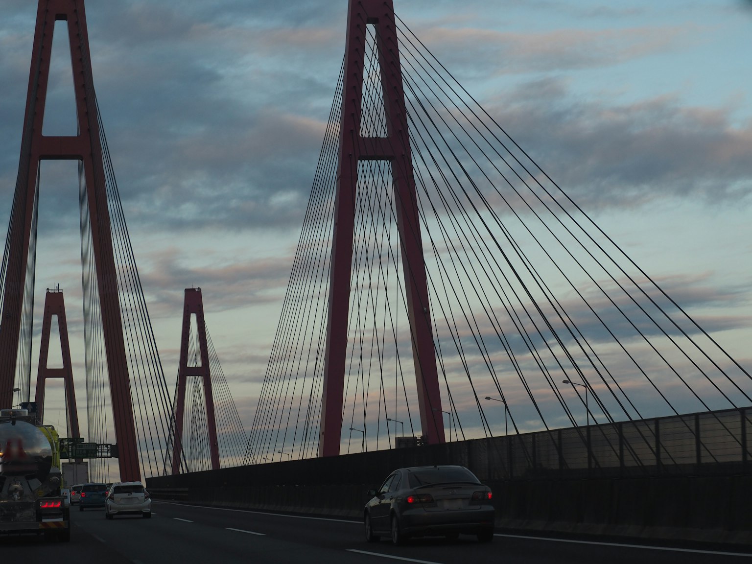 Puente atirantado rojo con una carretera y cielo nublado