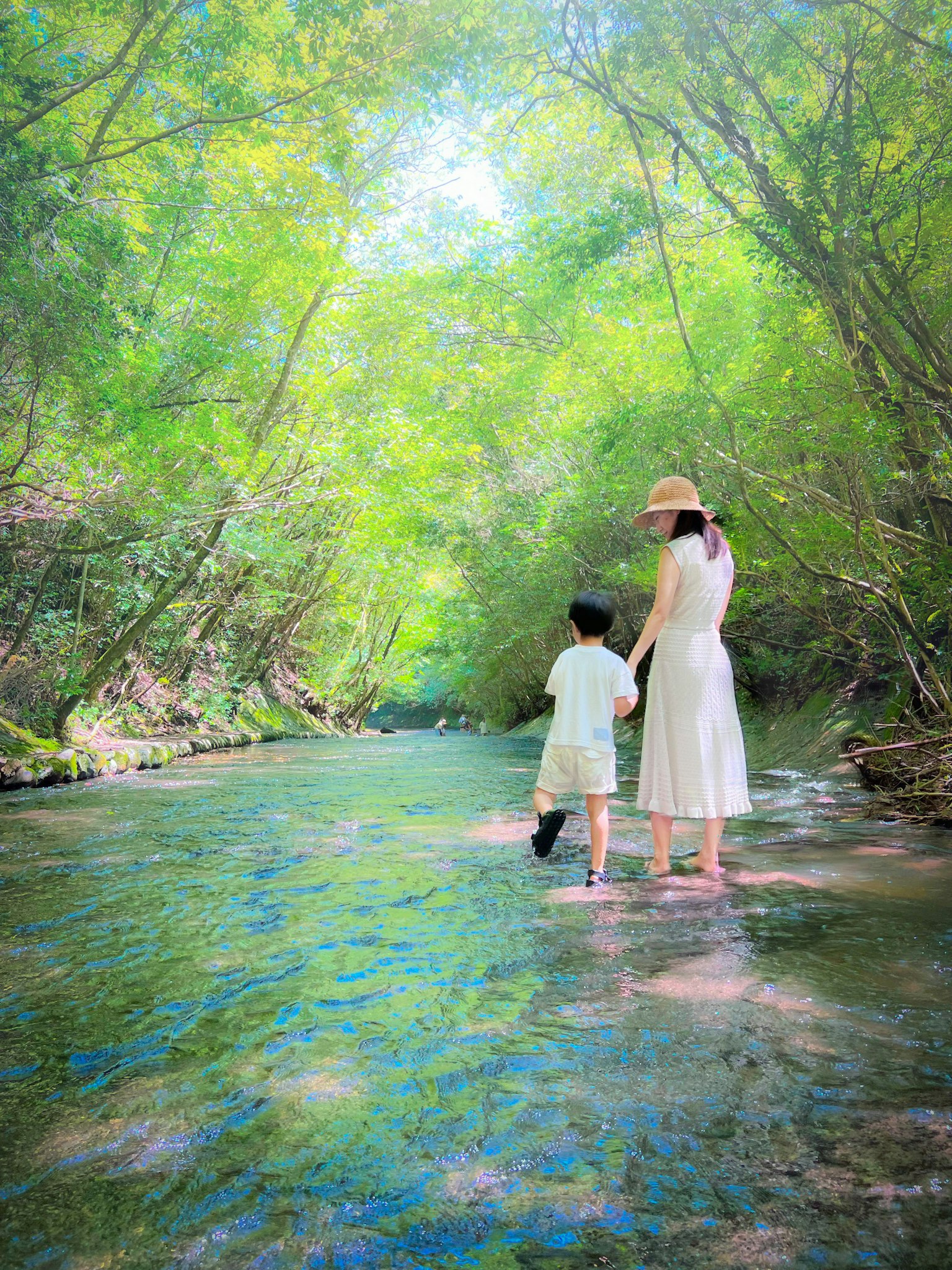 A mother and child wading in a stream surrounded by lush green trees