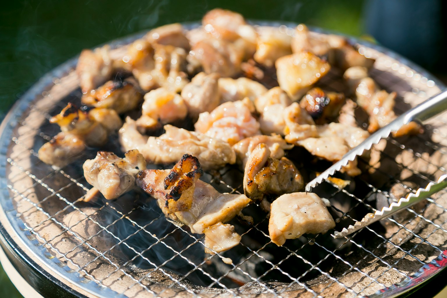 Grilled pieces of meat on a wire rack with smoke rising
