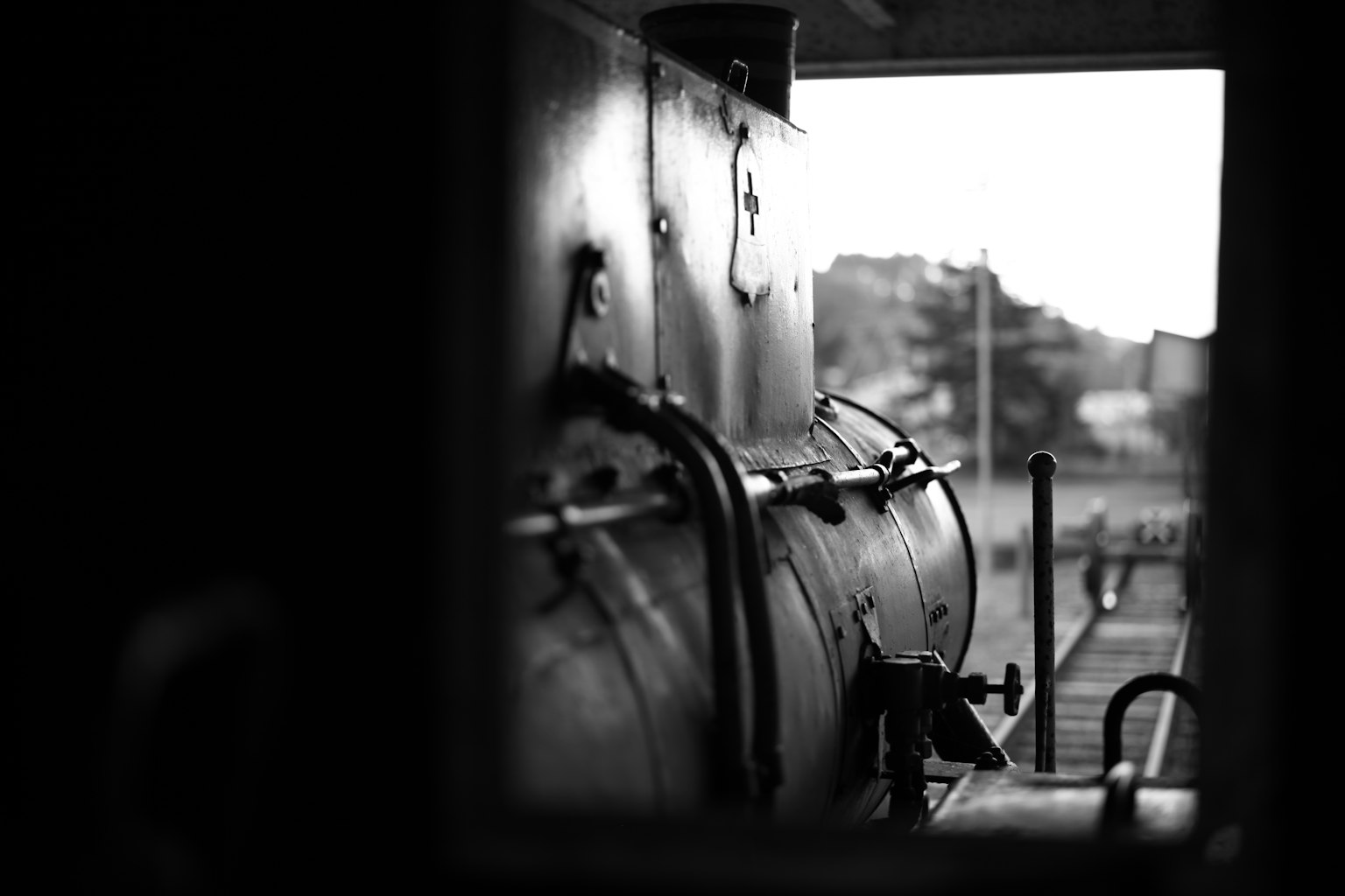 Immagine in bianco e nero di una locomotiva a vapore parzialmente visibile attraverso una finestra