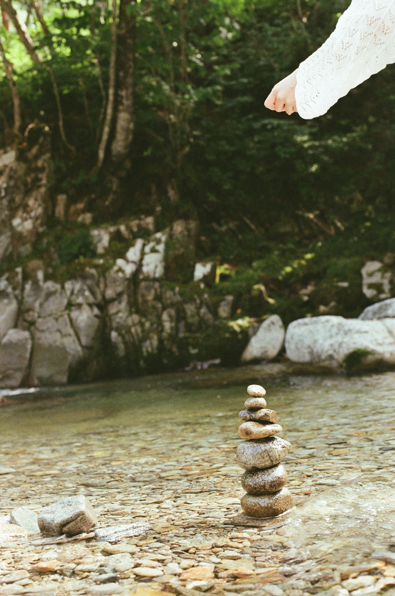 川のそばに積まれた石の塔とその近くで足を上げている人