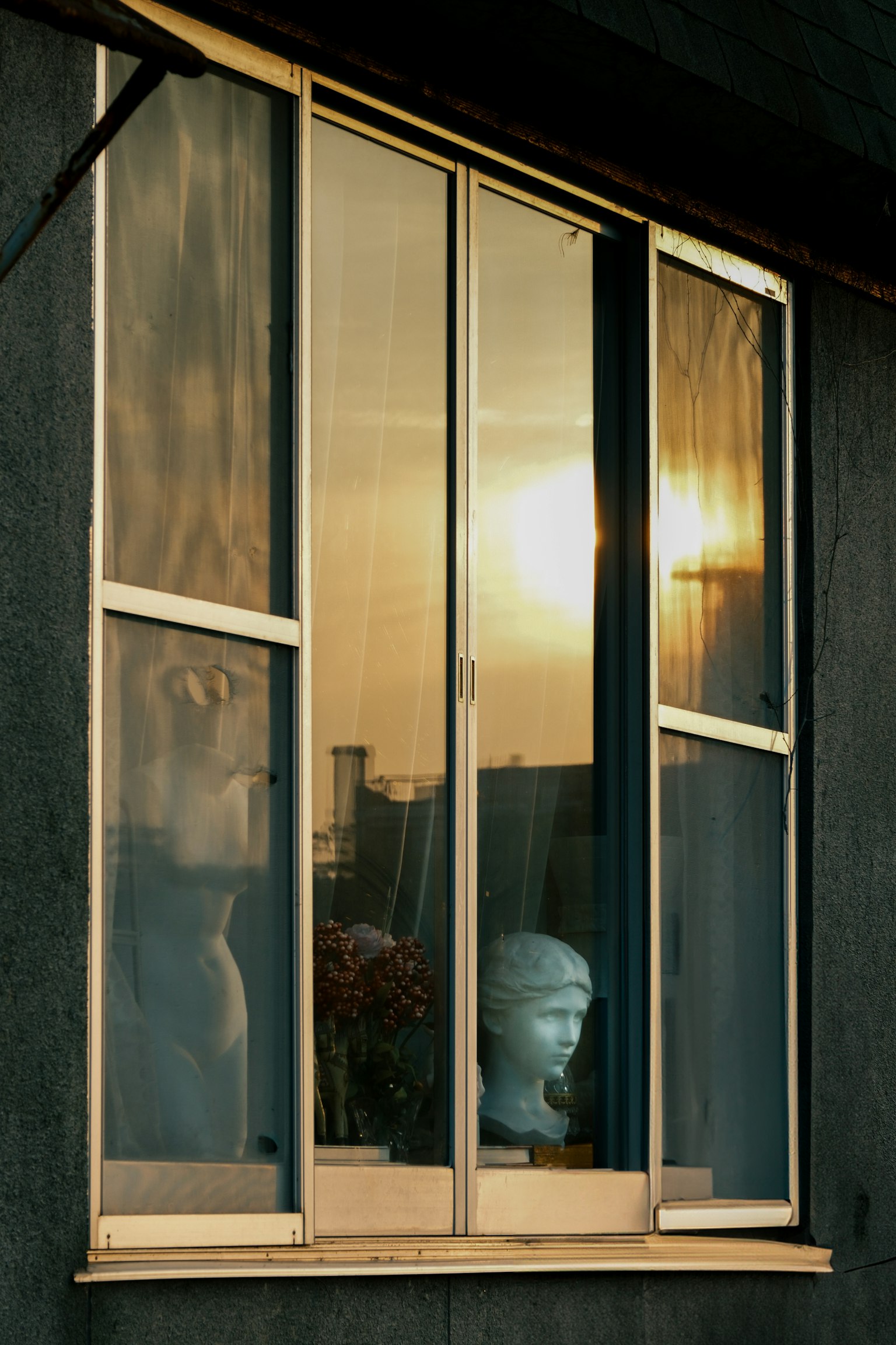 Reflexion des Sonnenuntergangs und eines Skulpturenkopfes in einem Fenster