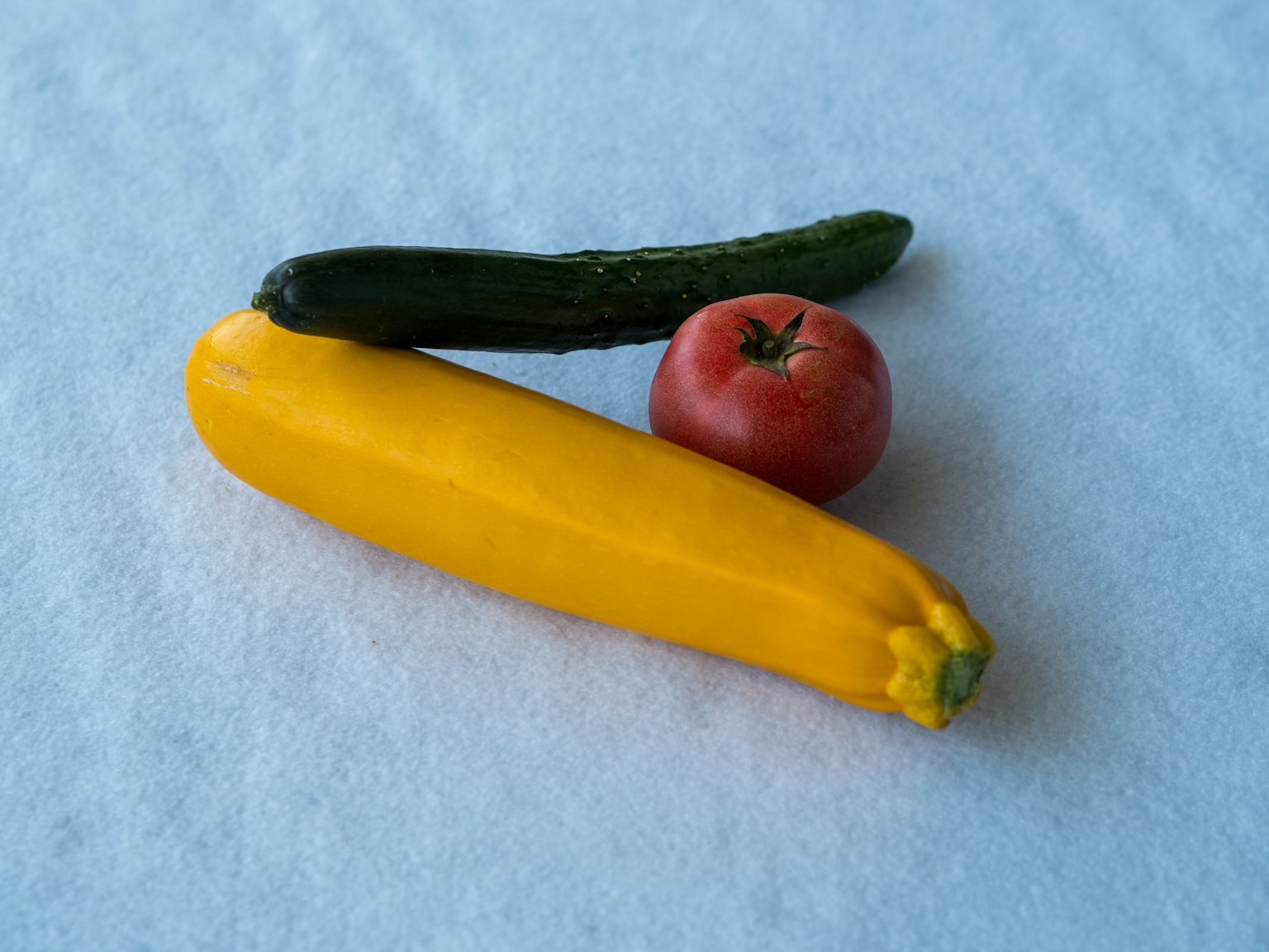 Un zucchini jaune, un concombre vert et une tomate rouge disposés ensemble