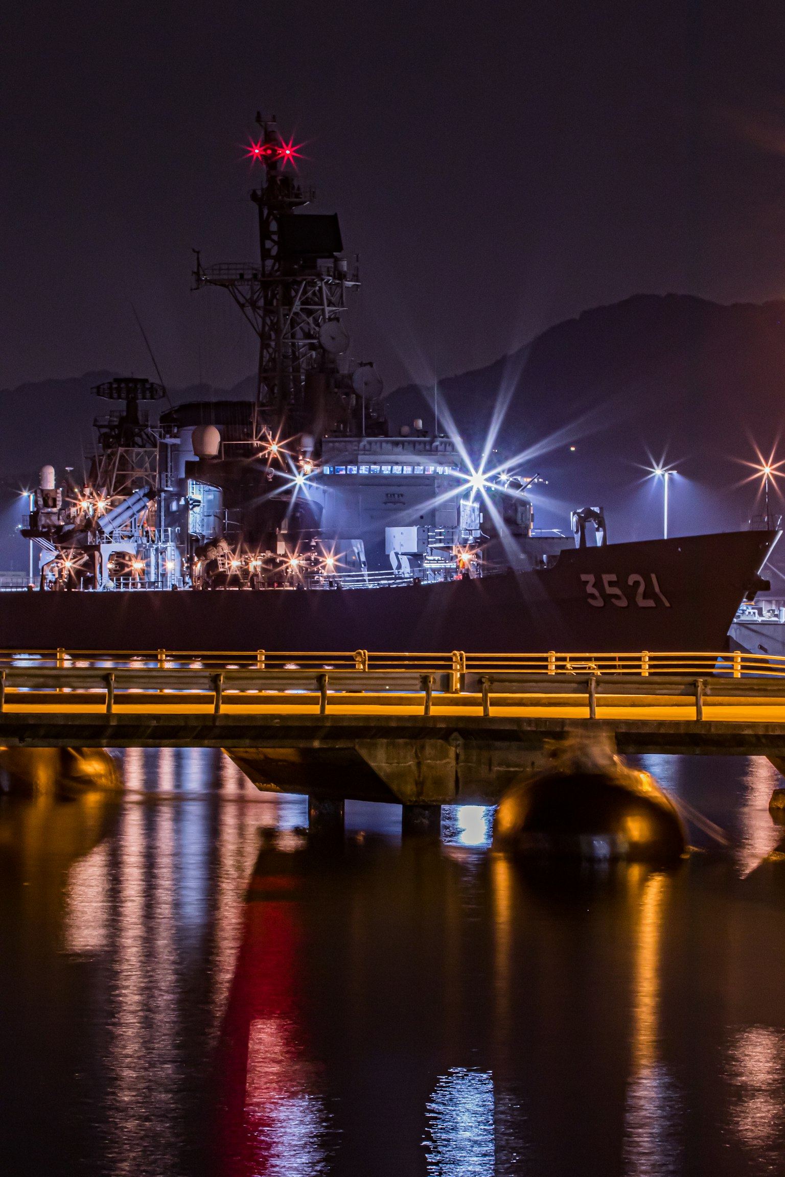 Ein Kriegsschiff bei Nacht mit hellen Lichtern, die sich im Wasser spiegeln
