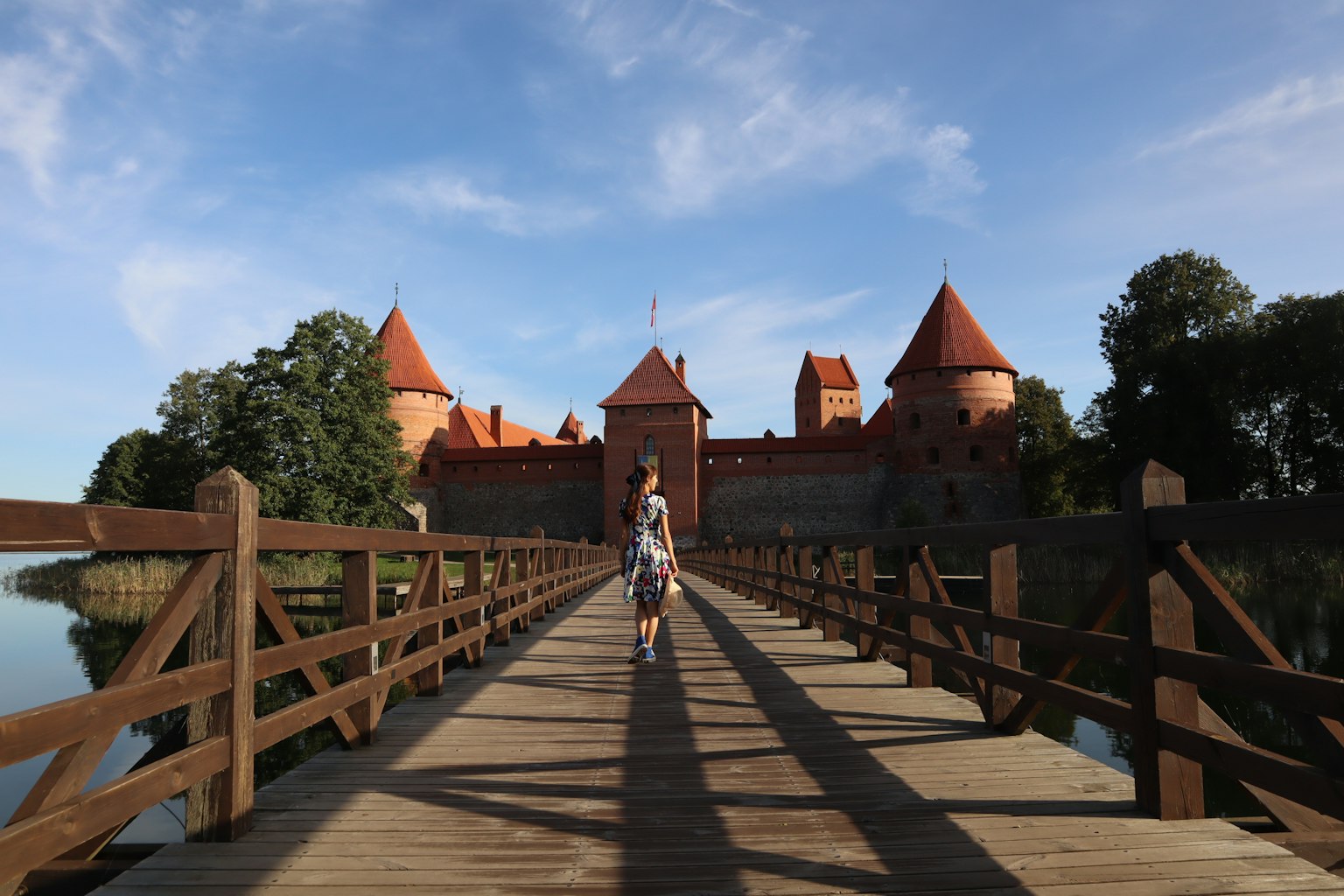 Eine Frau, die auf einer Holzbrücke über einen See läuft, mit einem roten Dachschloss im Hintergrund