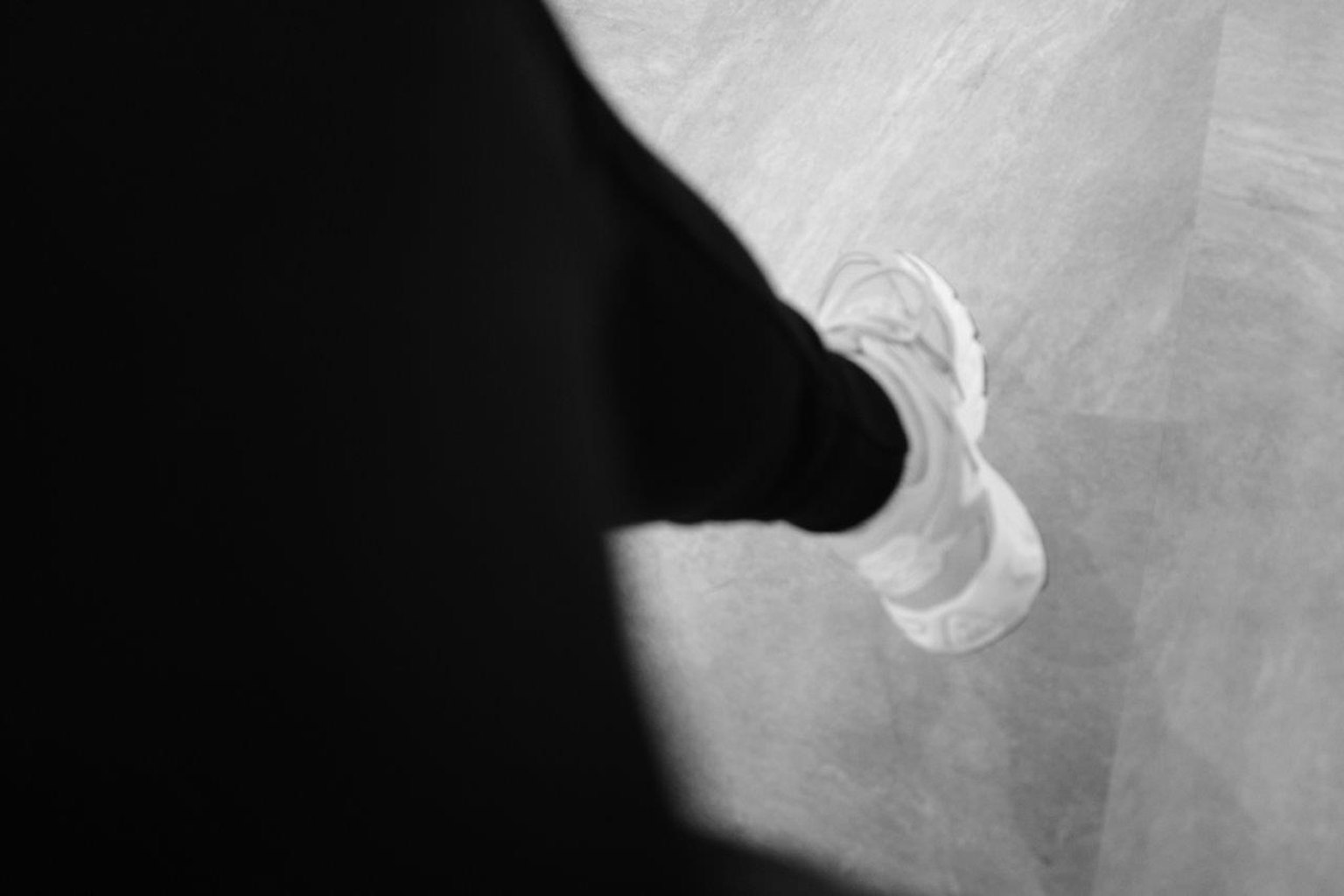 Sebuah kaki yang mengenakan sneaker putih di lantai dalam gambar hitam putih