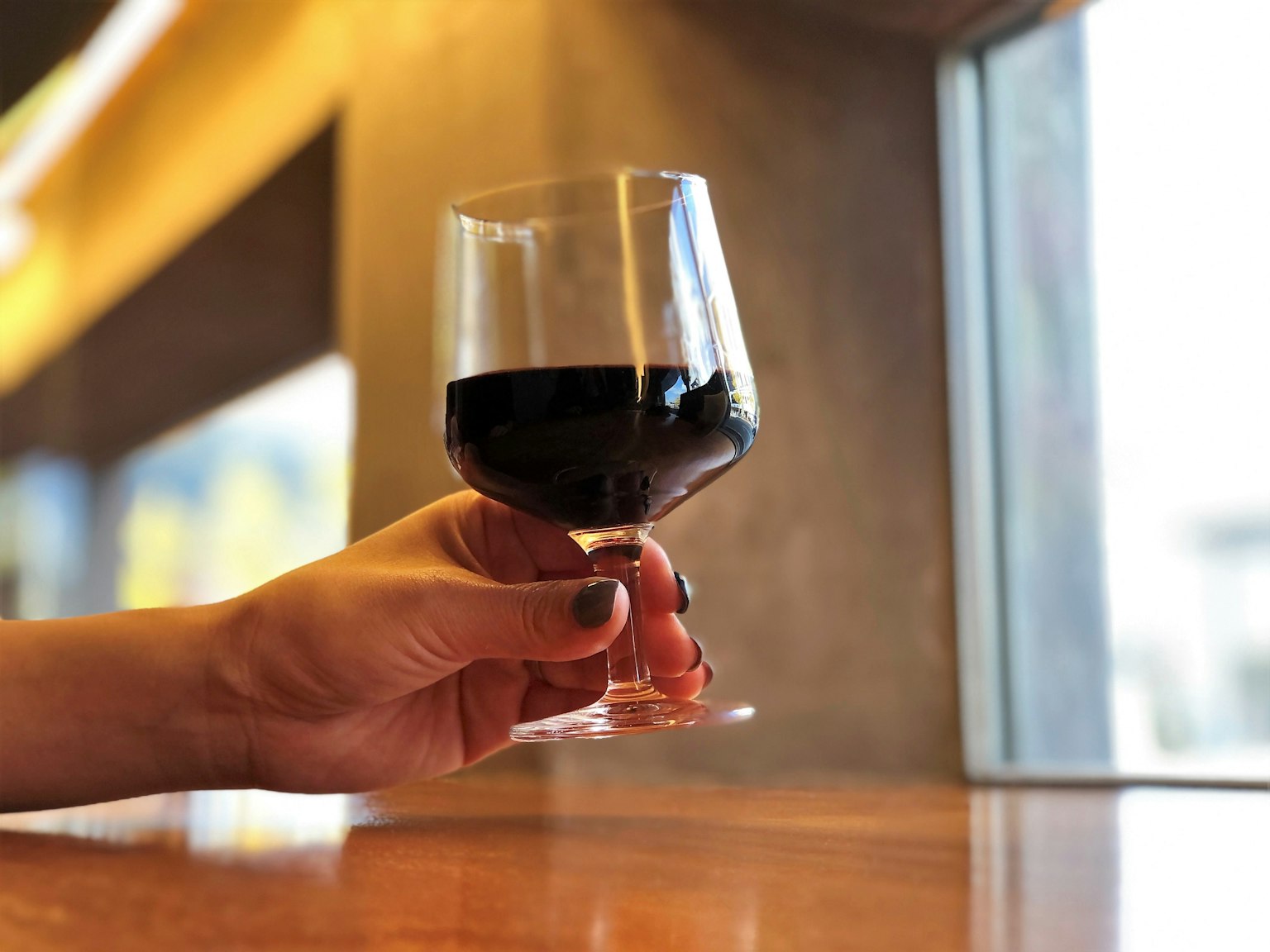 A hand holding a glass of red wine in a casual interior setting