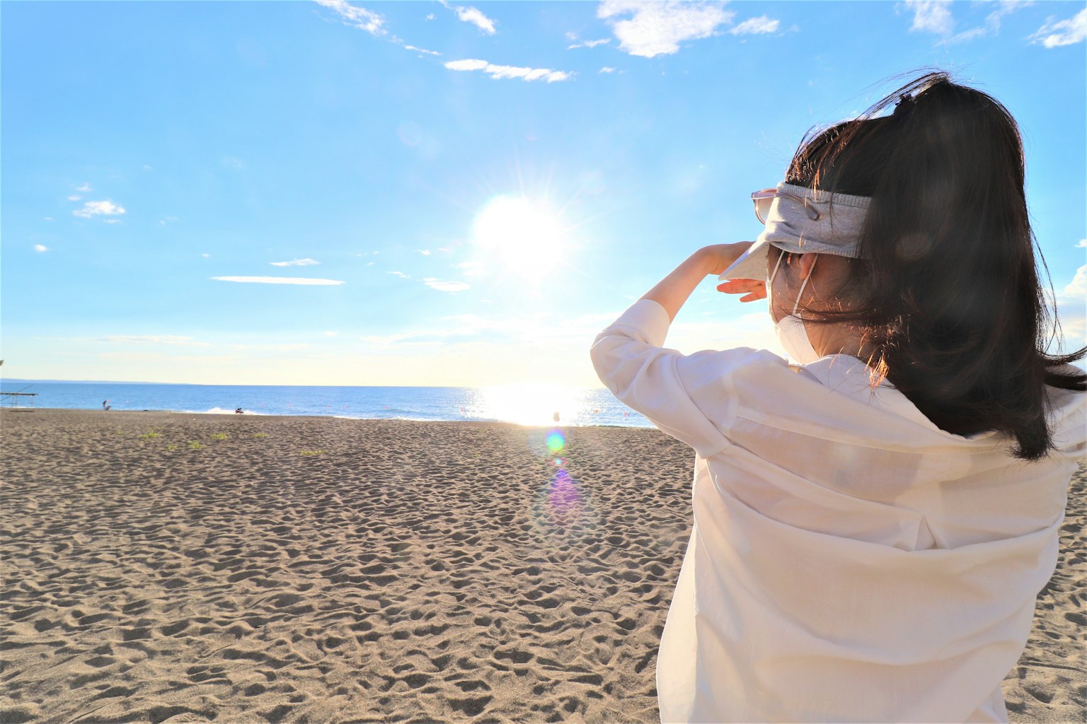 Mujer con camisa blanca observando la puesta de sol en la playa