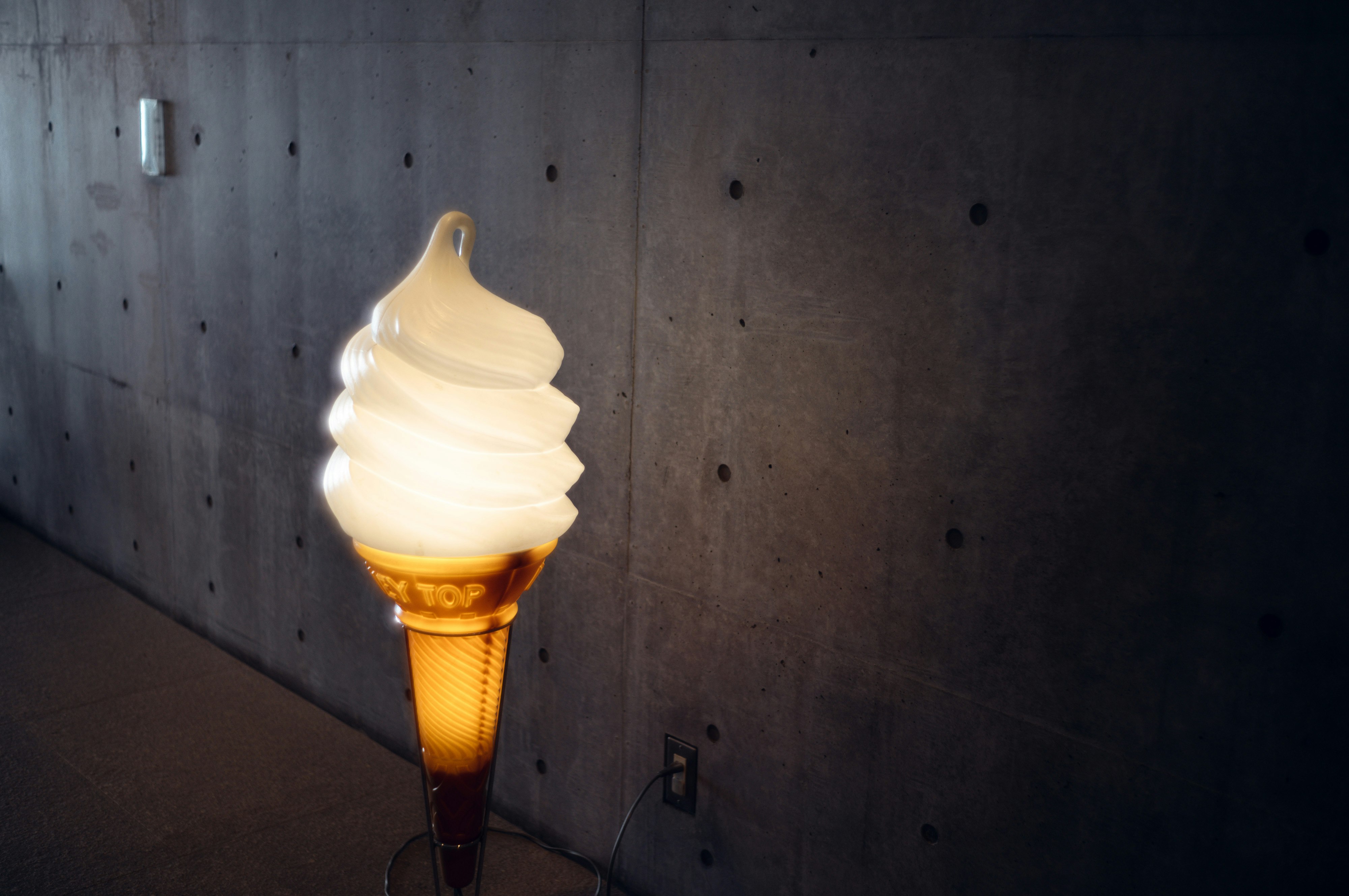 コンクリートの壁に照らされたソフトクリーム型のランプ