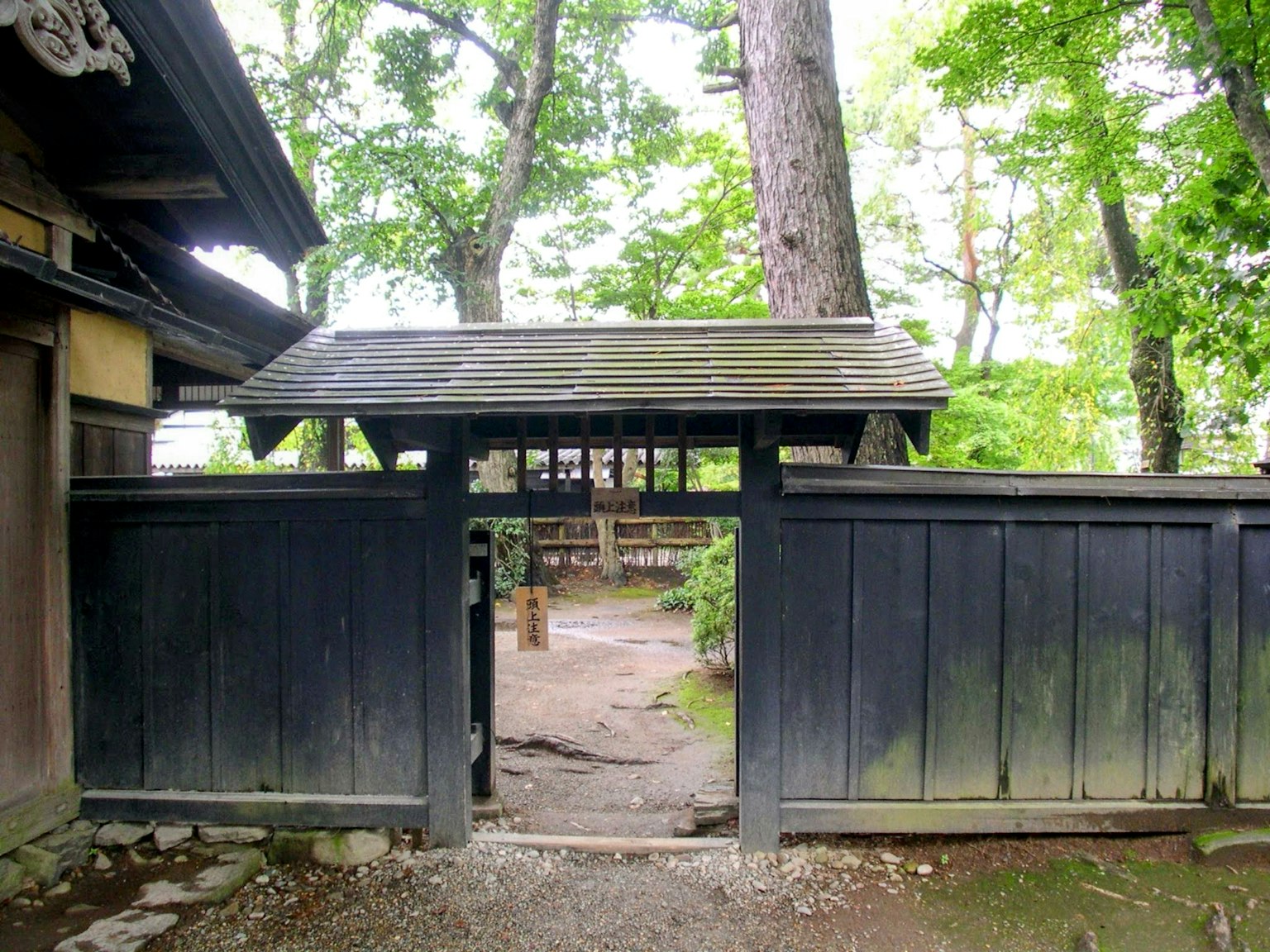 Black wooden gate leading to a lush green garden with trees