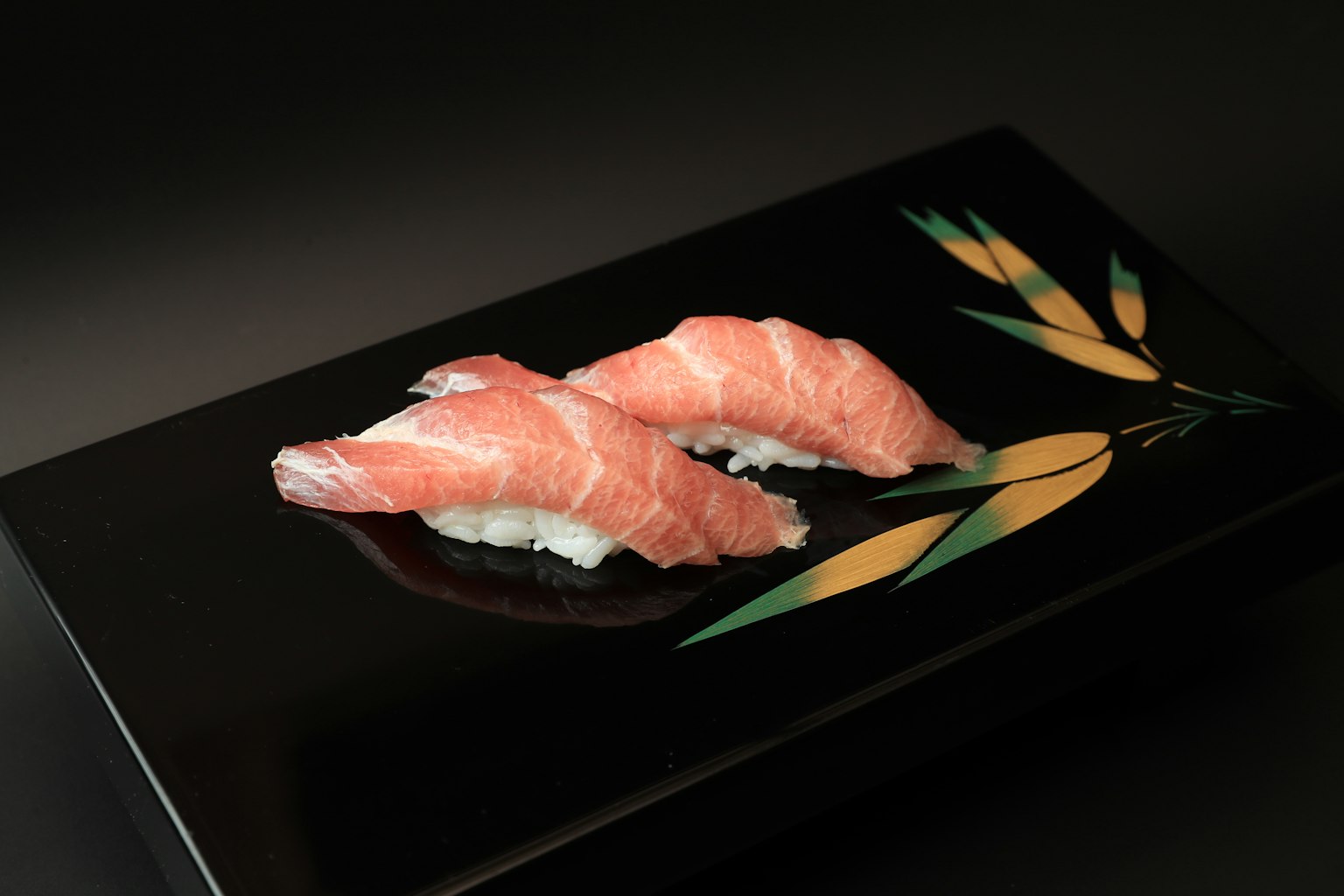 Hai miếng sushi cá hồi được sắp xếp đẹp mắt trên đĩa đen có họa tiết tre
